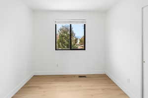 Bright room featuring a large window with black framing, wood-finish flooring, white walls, white baseboards, and a white closet door