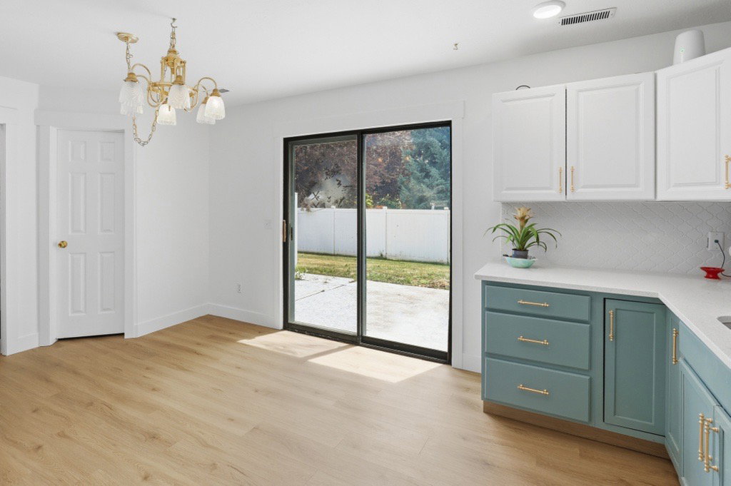 Kitchen area featuring wood-finish flooring, two-tone cabinetry with gold-toned hardware, white countertops, and a white subway tile backsplash