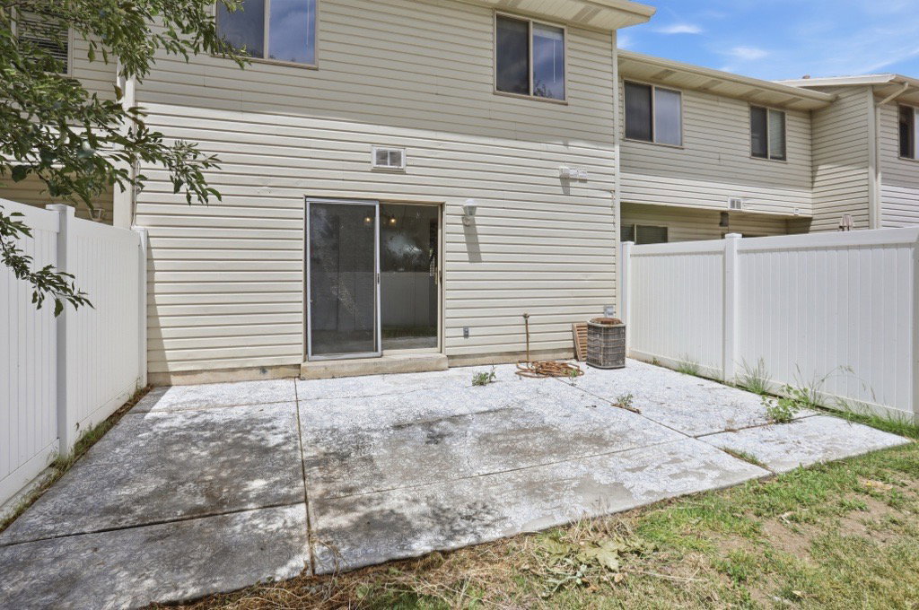 Rear exterior with a concrete patio, sliding glass door, and white privacy fencing