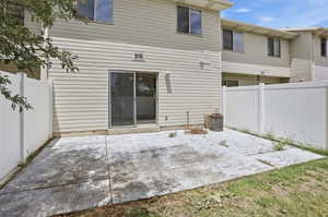 Rear exterior with a concrete patio, sliding glass door, and white privacy fencing