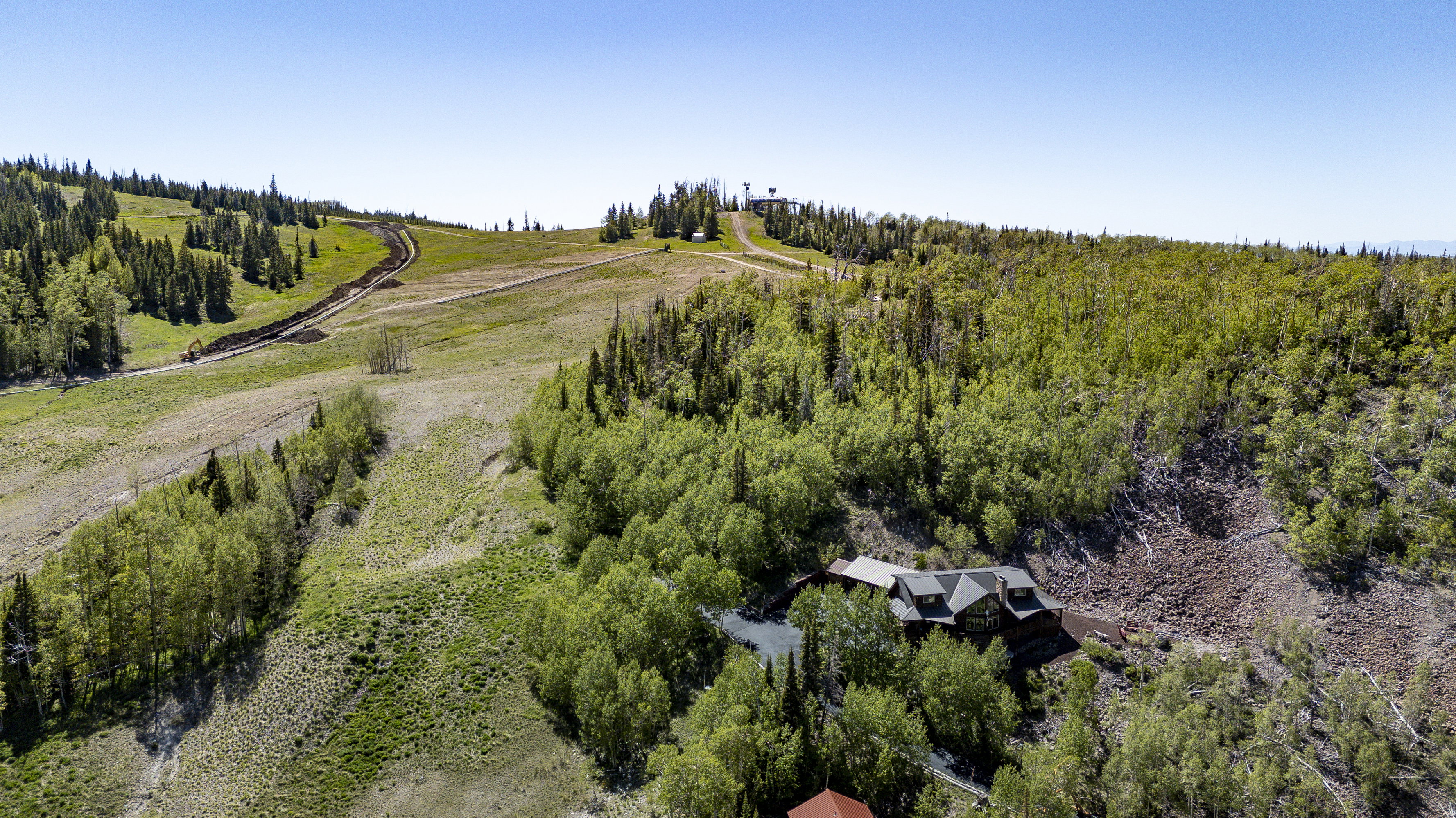 Hillside property surrounded by mature trees, featuring a multi-level structure and a gravel drive