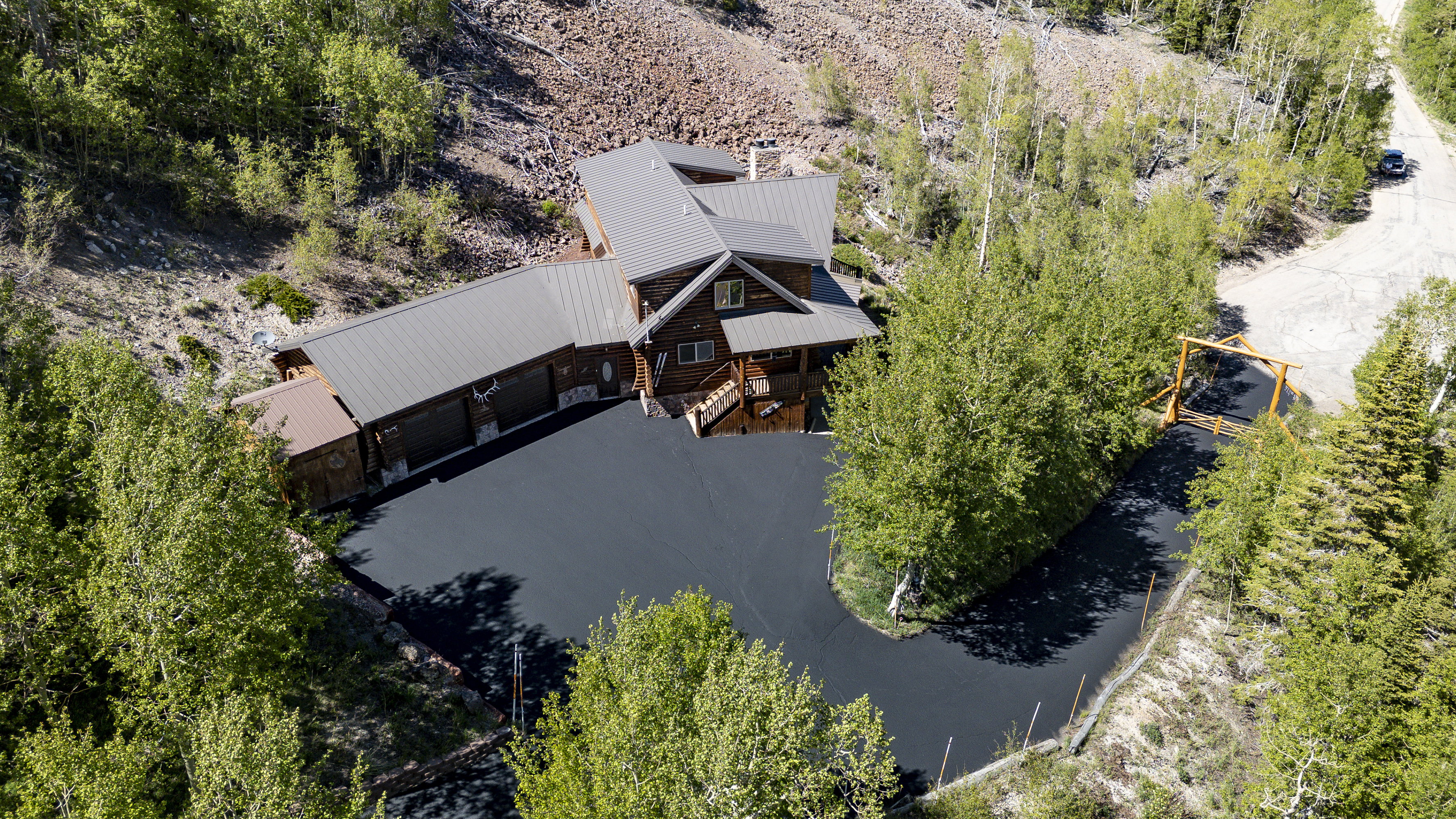 Log-style residence with a dark metal roof, featuring a paved driveway and surrounding mature trees