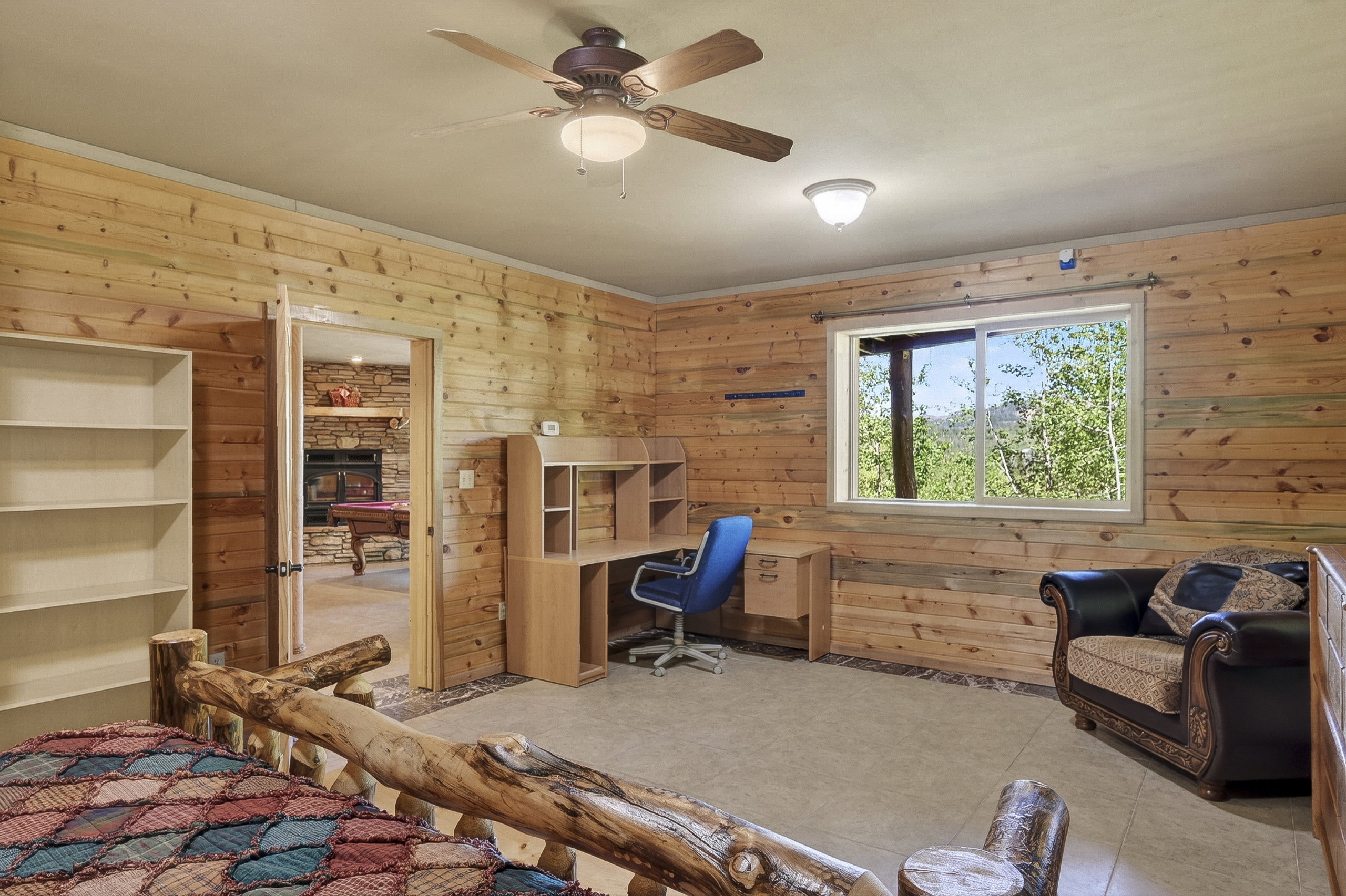 Room featuring extensive wood paneling, a large window with natural light, a ceiling fan with integrated lighting, and tile flooring