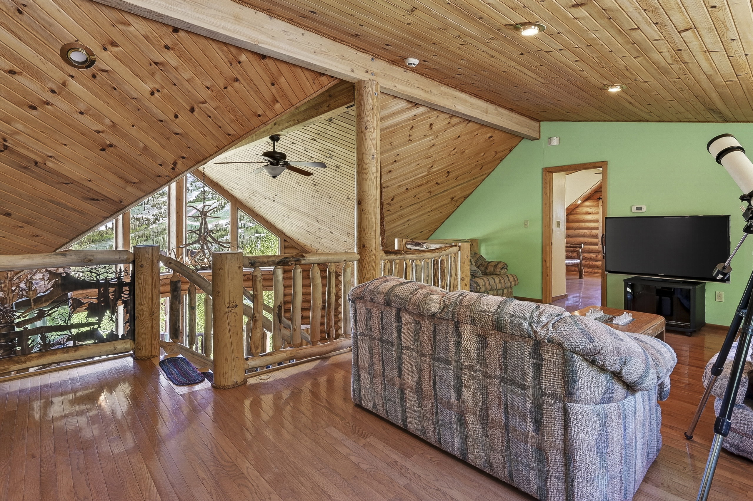 Open-concept living space featuring wood-finish flooring, natural wood paneled ceilings, and log railing accents