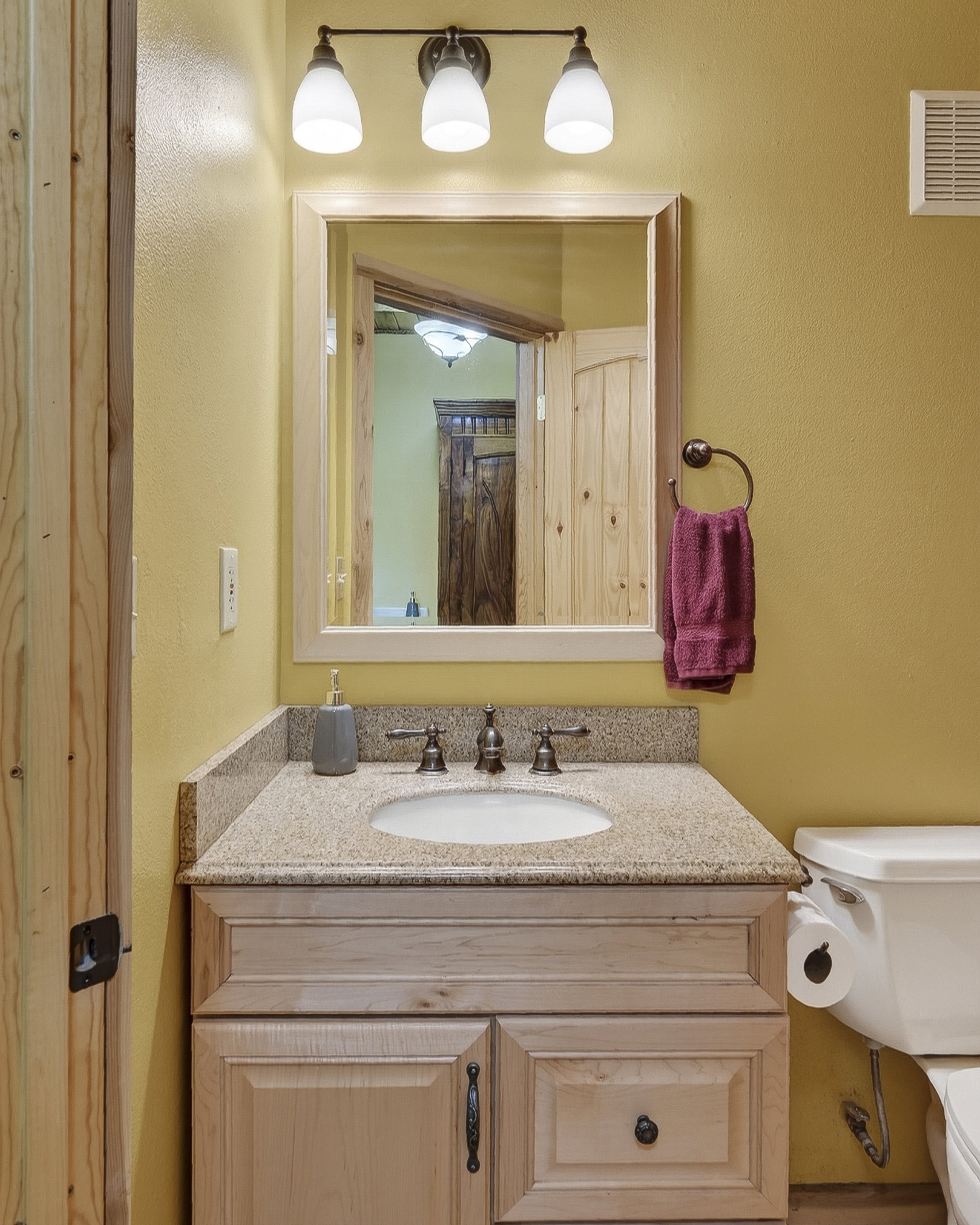 Vanity featuring a light wood cabinet, granite-look countertop, and bronze-finish faucet