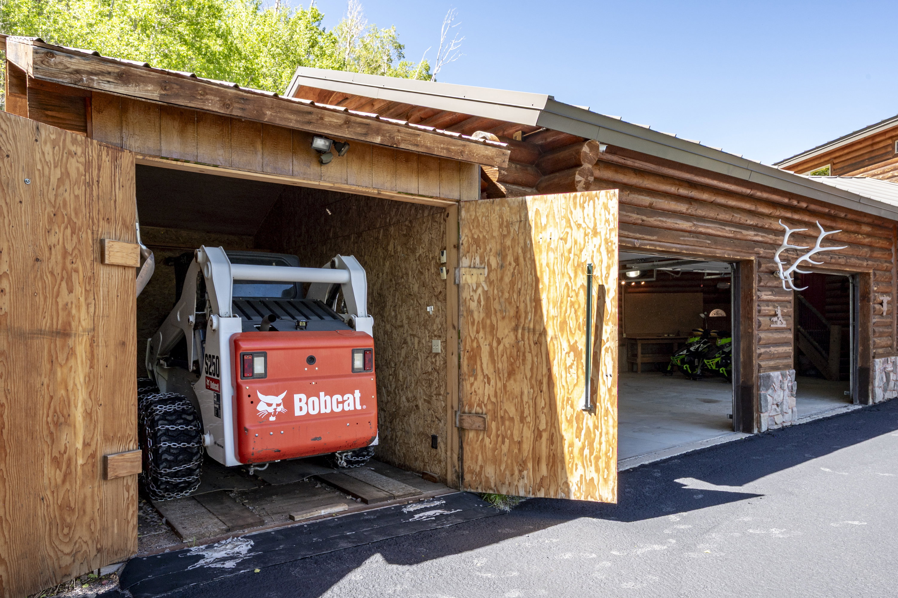 Multi-bay garage and storage structure featuring log siding, stone accents, and wood-paneled doors