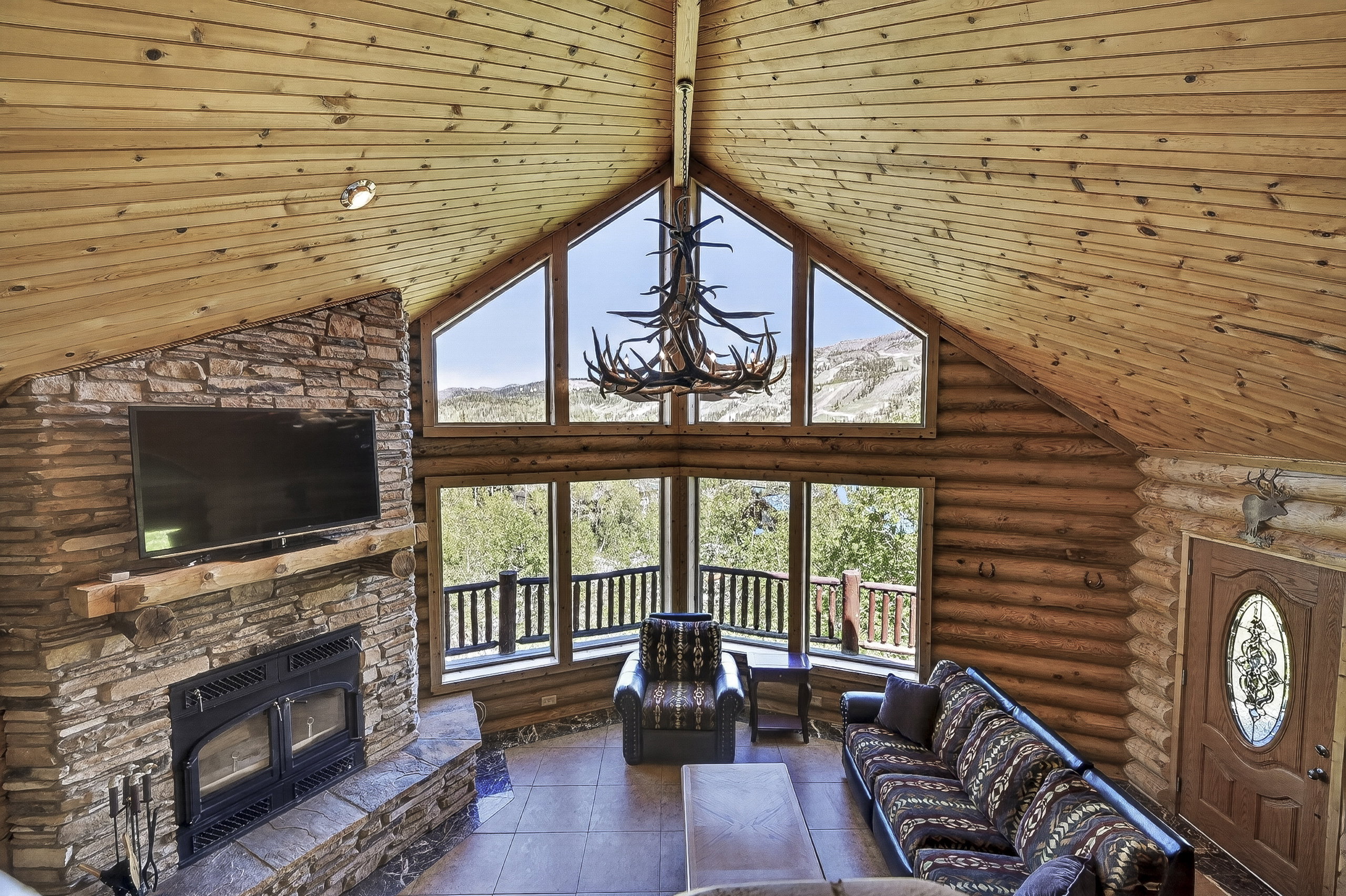 Vaulted ceiling with wood-finish planks, stone-clad fireplace with wood mantle, and a large window array with mountain scenery
