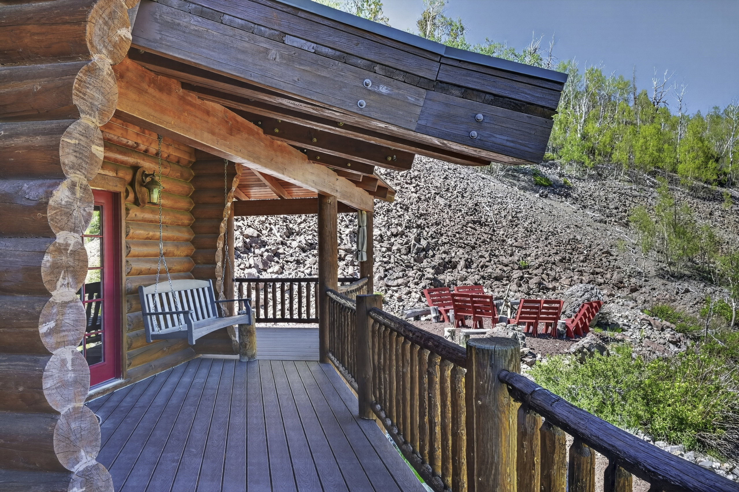 Expansive log cabin porch featuring a durable composite deck, rustic log railings, and a red entry door