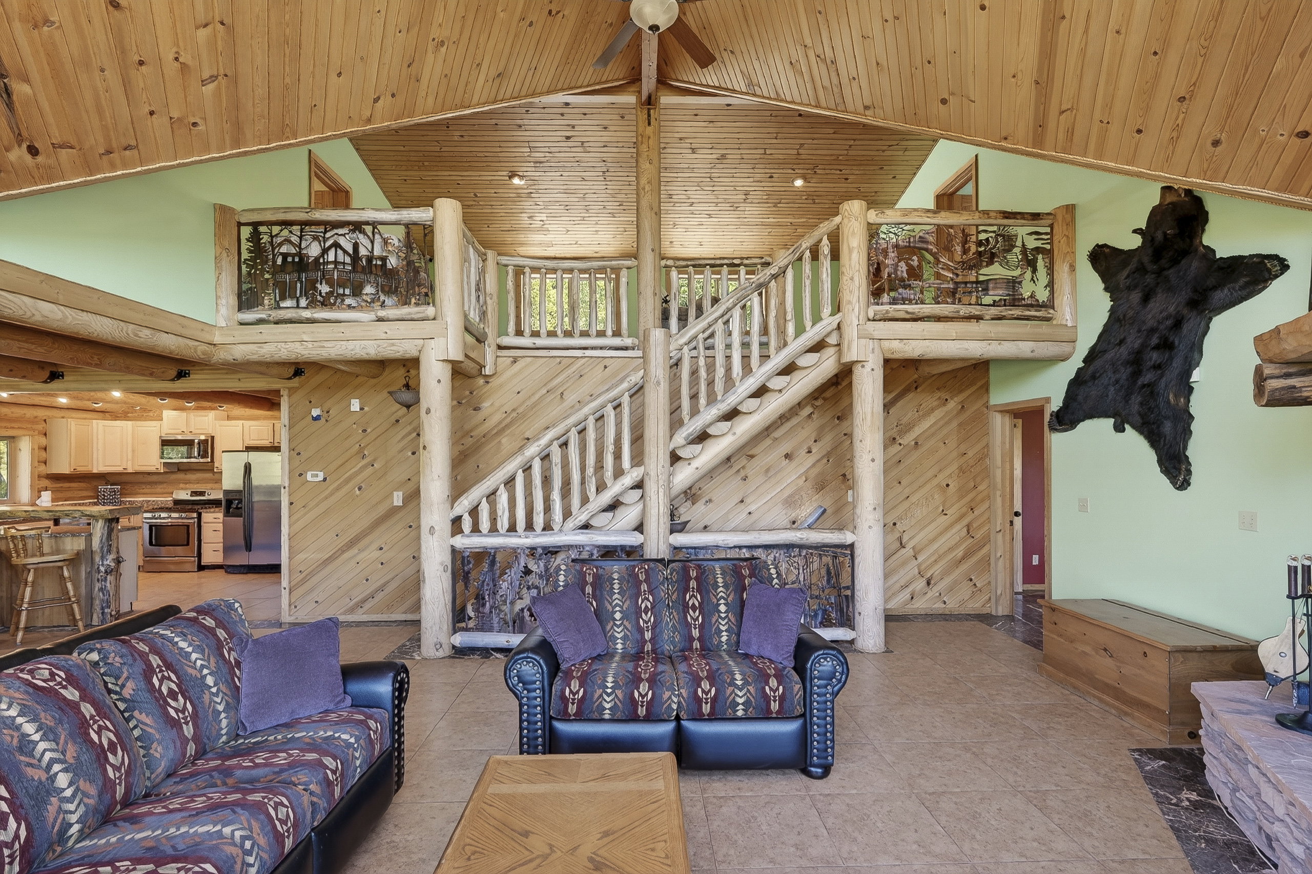 Great room with a vaulted wood-finish ceiling, exposed wood beams, and a prominent wood staircase leading to an upper loft