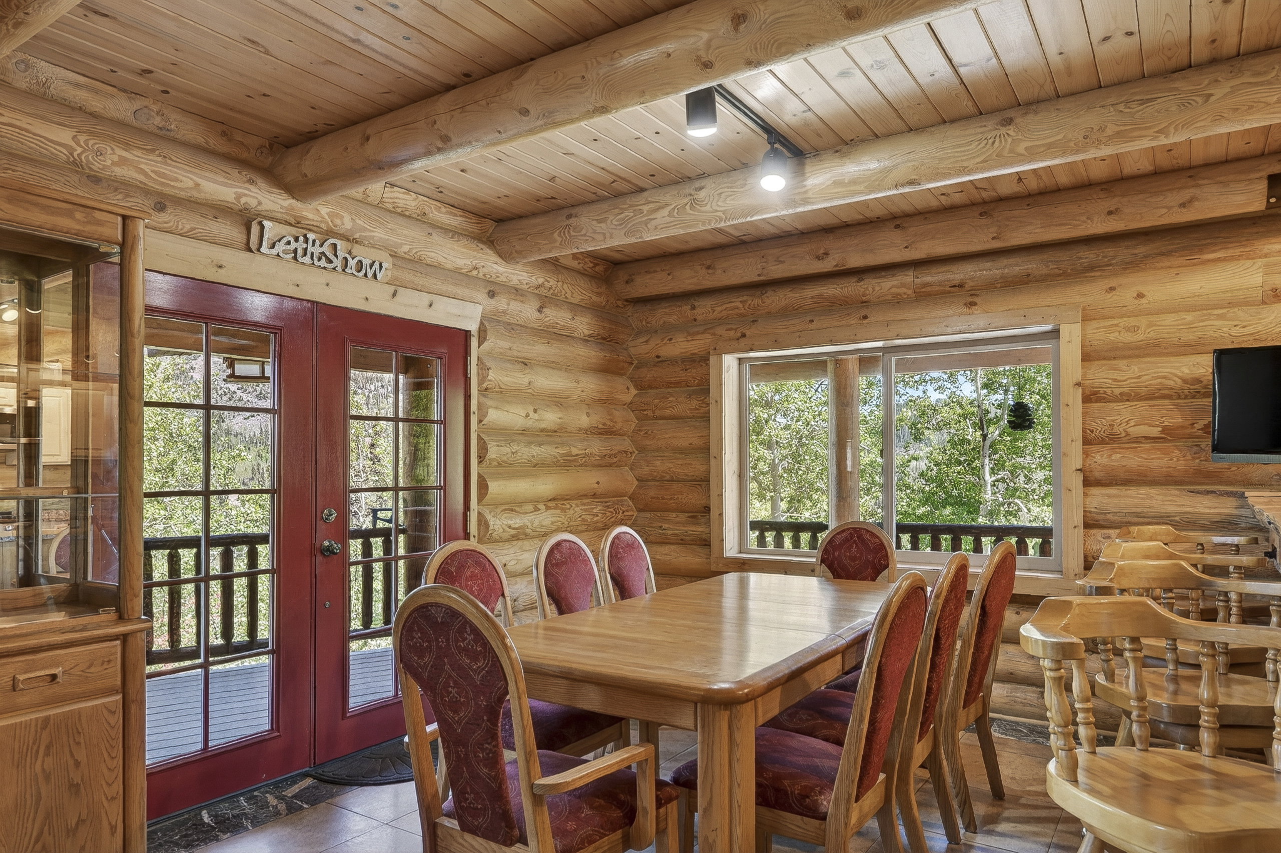 Interior featuring log walls and ceiling, exposed timber beams, track lighting, and a large picture window