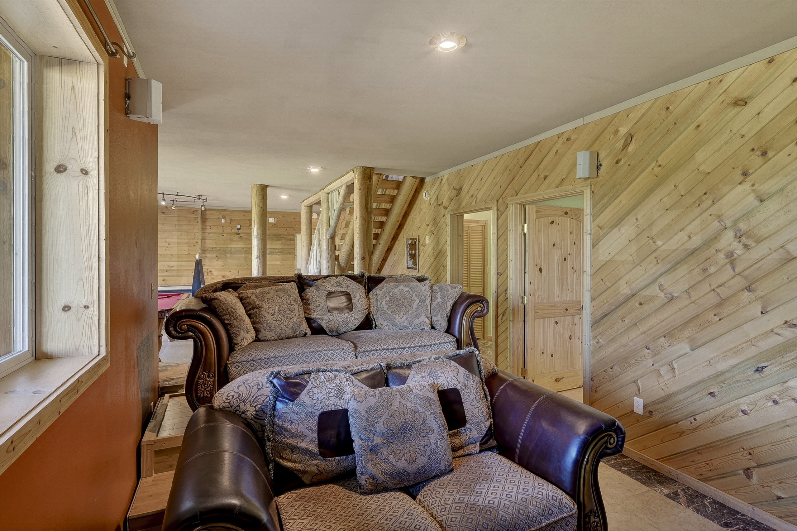 Spacious room featuring extensive wood paneling, wood-finish flooring, recessed lighting, and a white-framed window