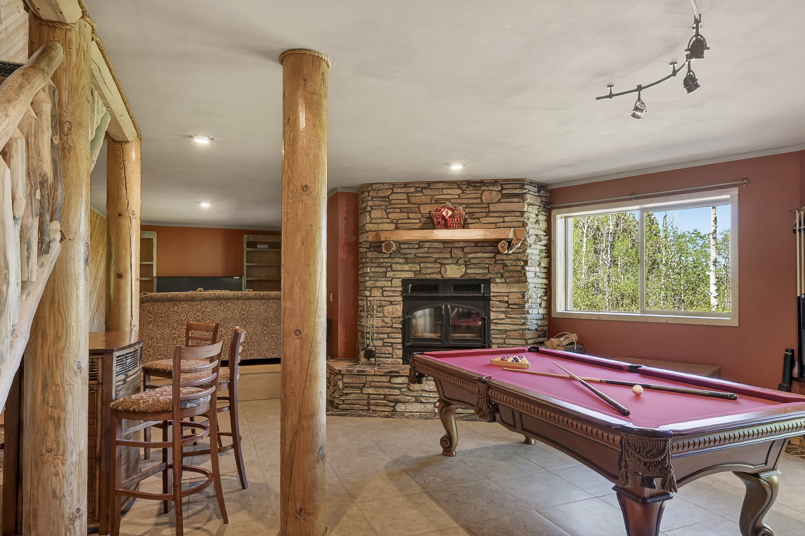 Spacious recreation room featuring a stone fireplace with hearth, a built-in bar, and log structural columns