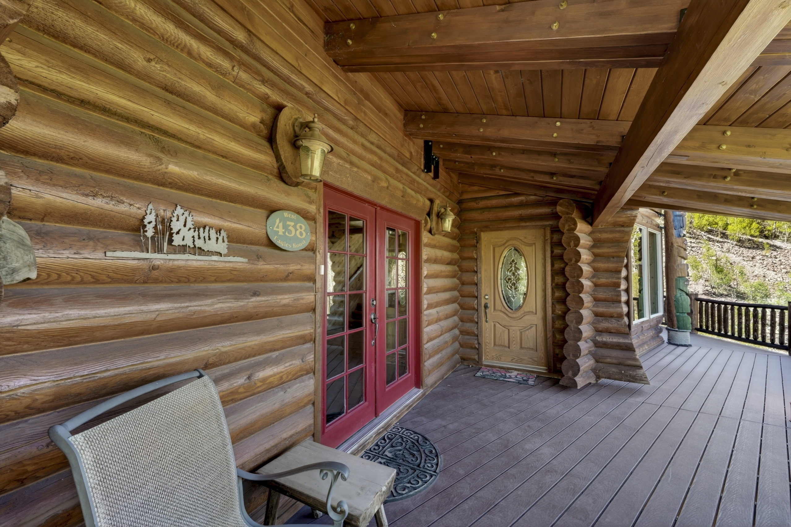 Log cabin exterior featuring a covered porch with wood-finish decking, exposed wood beams, and a decorative wood wall sconce