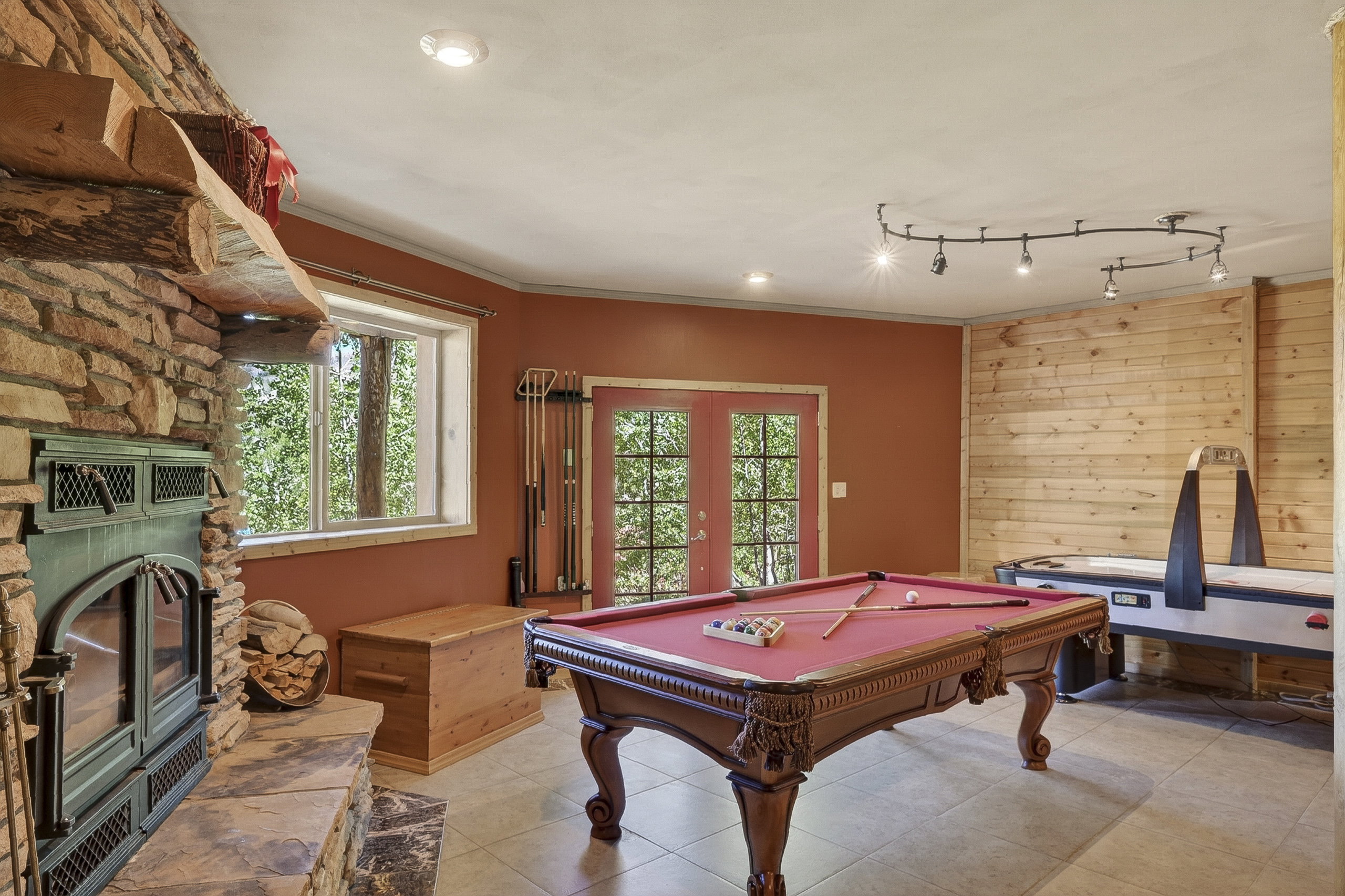 Entertainment room featuring a stone-clad fireplace with wood stove insert, tile flooring, and a wood accent wall