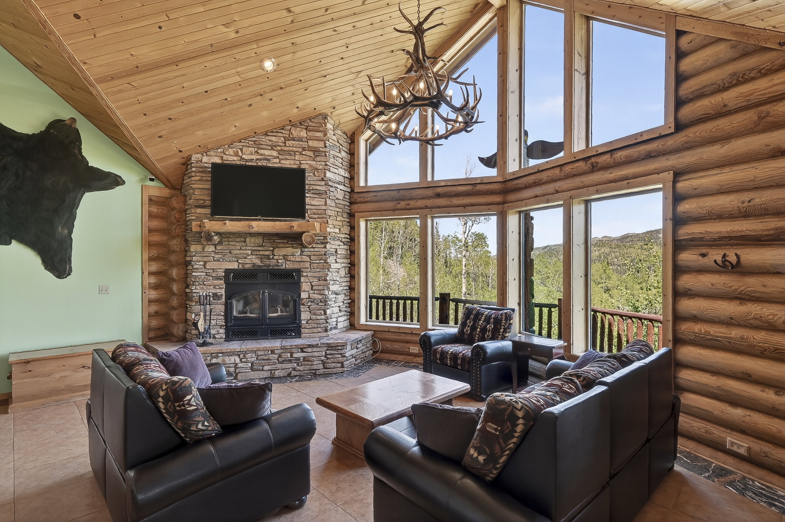 Expansive living area featuring soaring wood-paneled ceilings, a floor-to-ceiling stone fireplace, and log wall construction