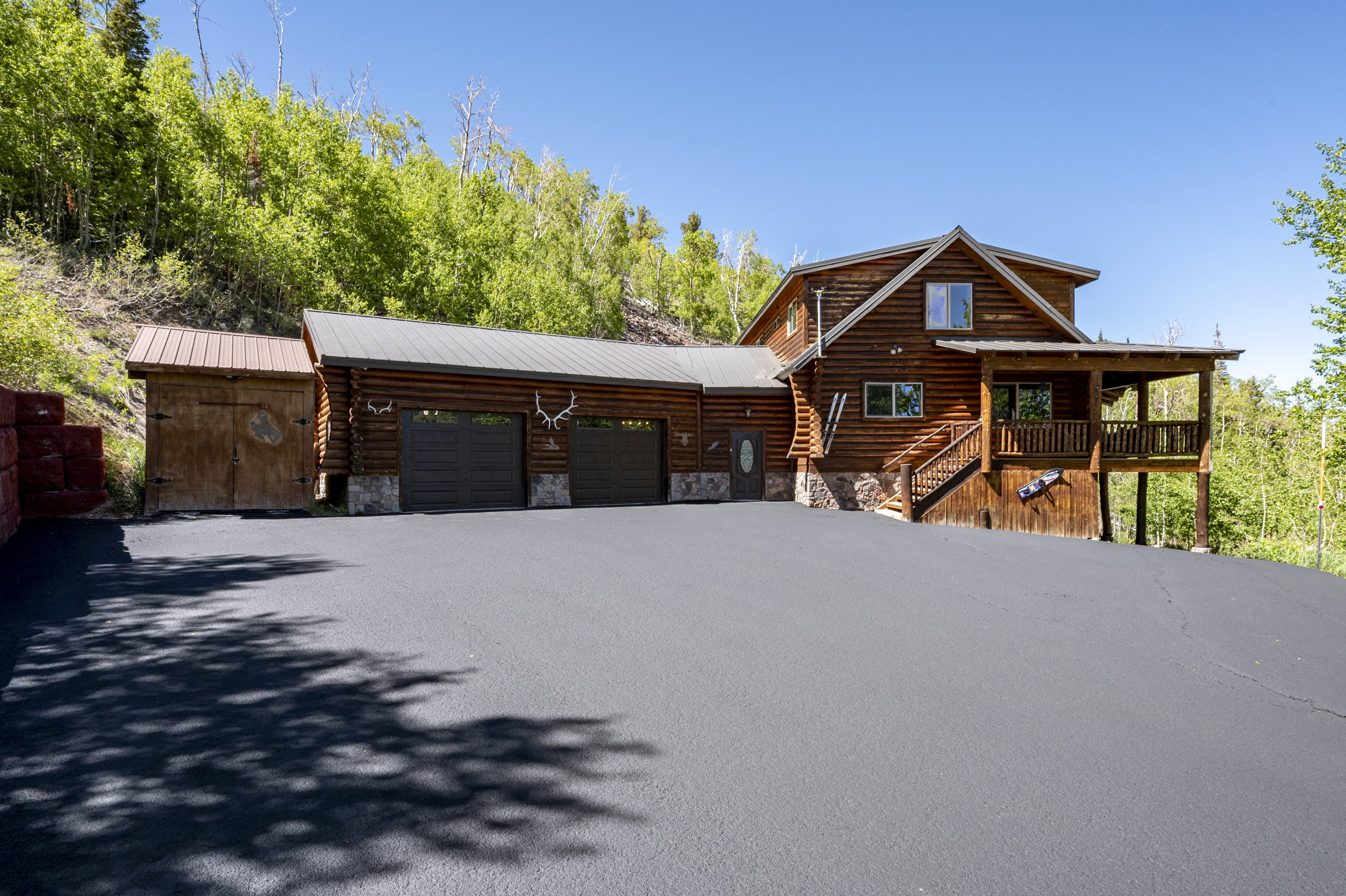 Log cabin style home featuring a covered front porch, a two-car garage with dark paneled doors, and an additional detached shed with a metal roof