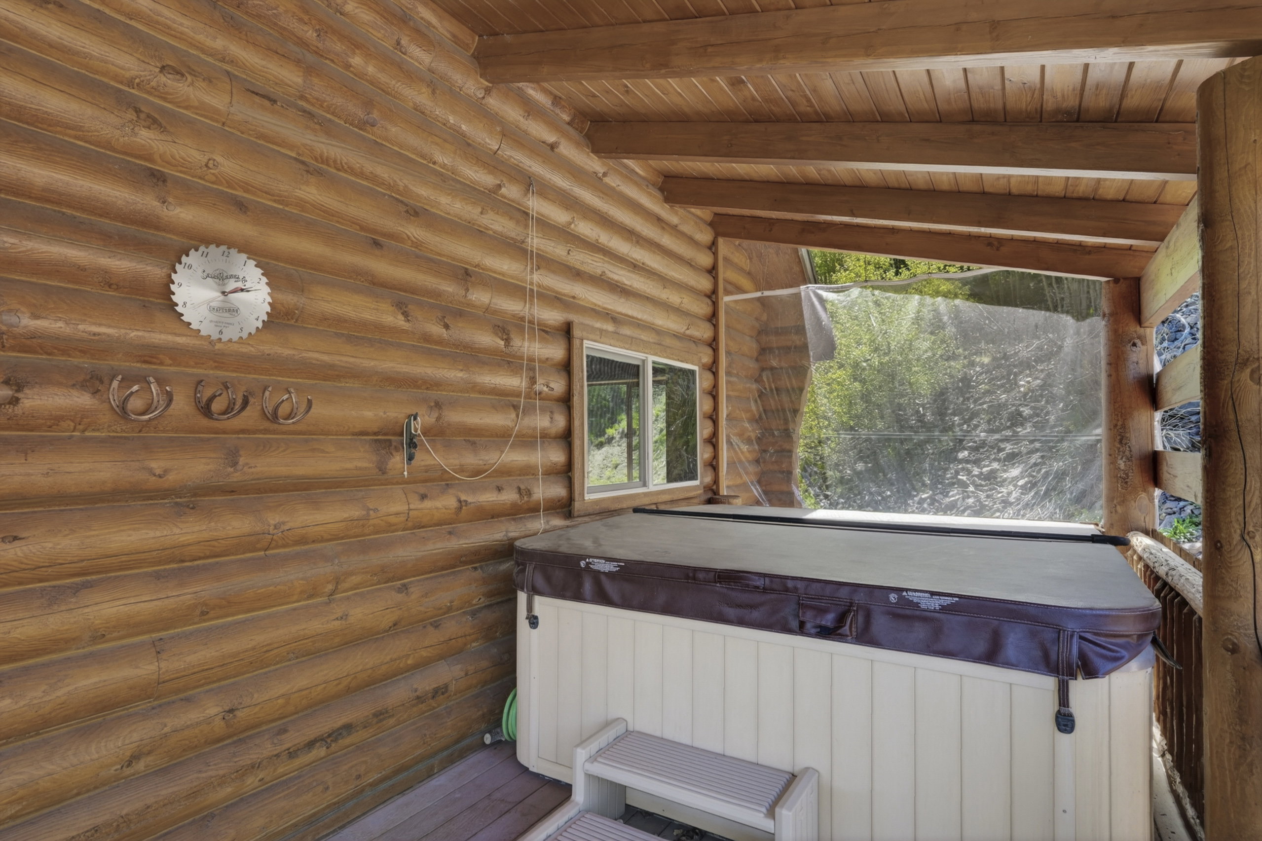 Covered exterior patio featuring a spa with cover, log walls, wood ceiling beams, and a window