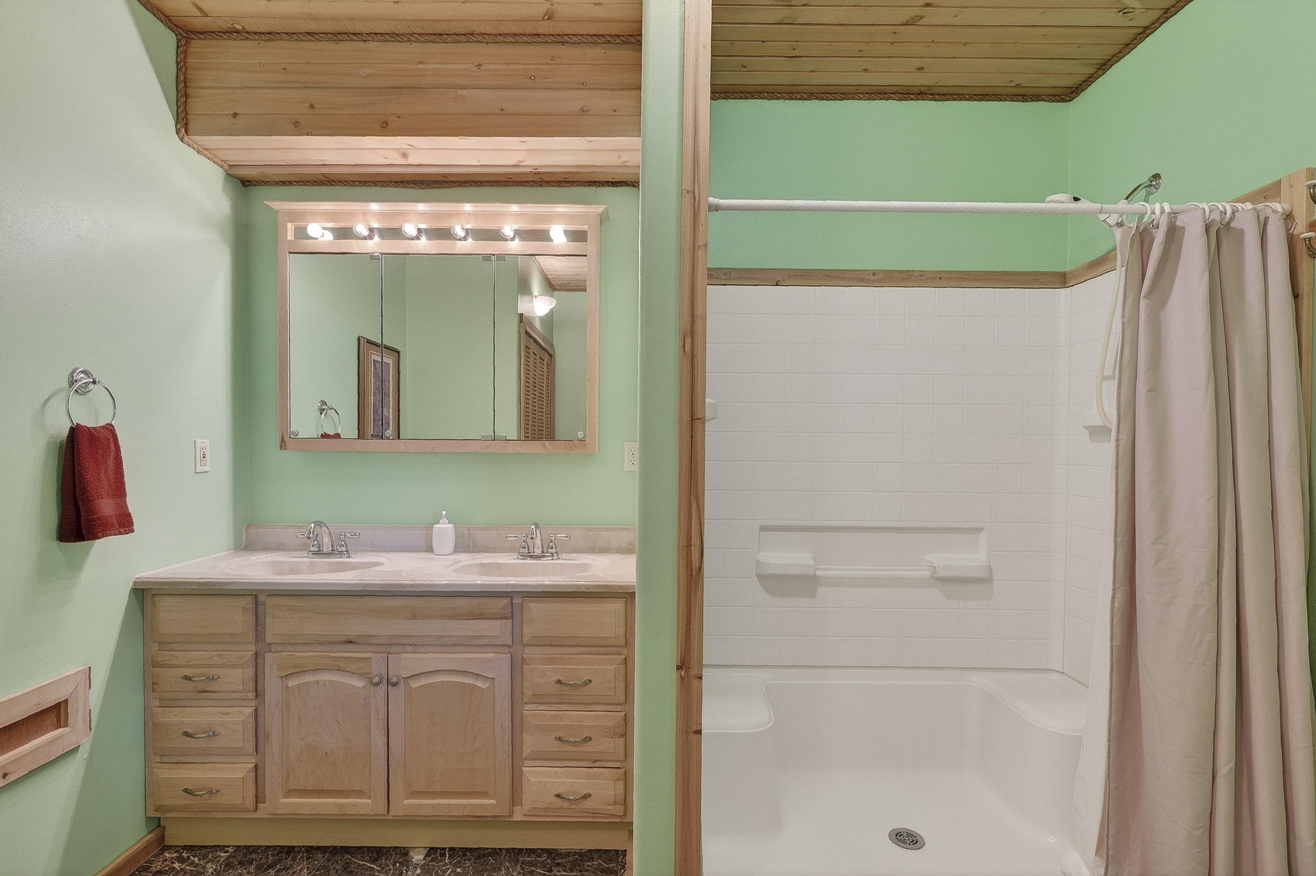 Bathroom featuring a dual-sink vanity with light wood cabinetry and a framed mirror with integrated lighting