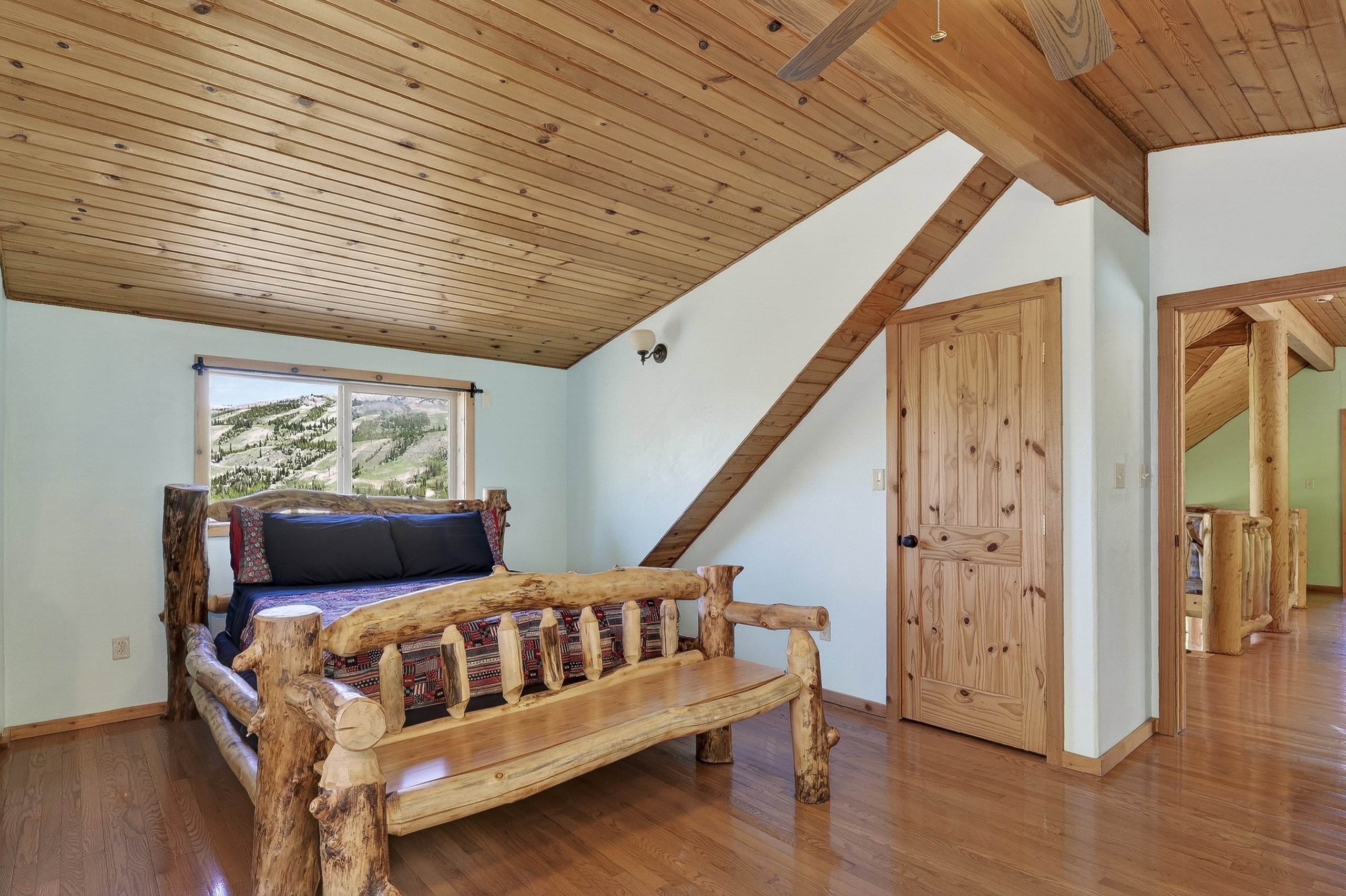 Room featuring wood-finish flooring, a sloped wood-paneled ceiling, a window with mountain scenery, a wood-paneled door, and exposed wood beams