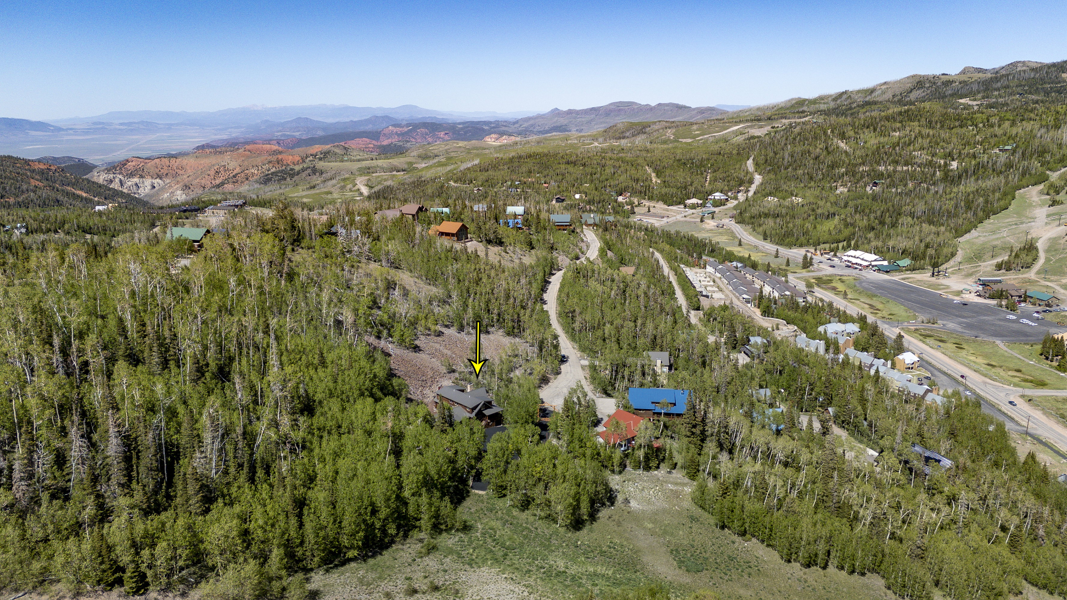 Mountain property surrounded by dense forest, featuring a prominent red roof and a rustic exterior