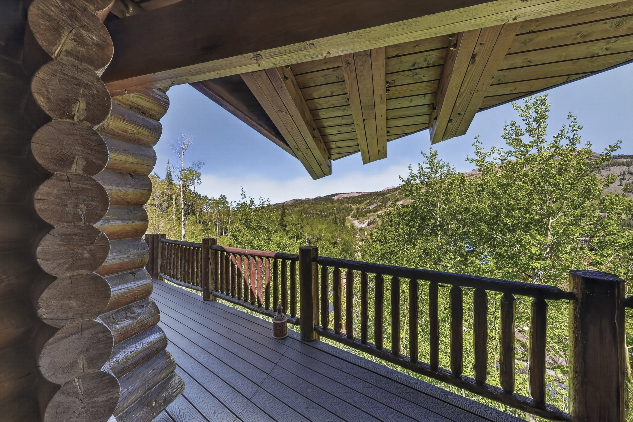 Rustic log construction balcony featuring a composite deck surface, log railing, and exposed wood ceiling beams