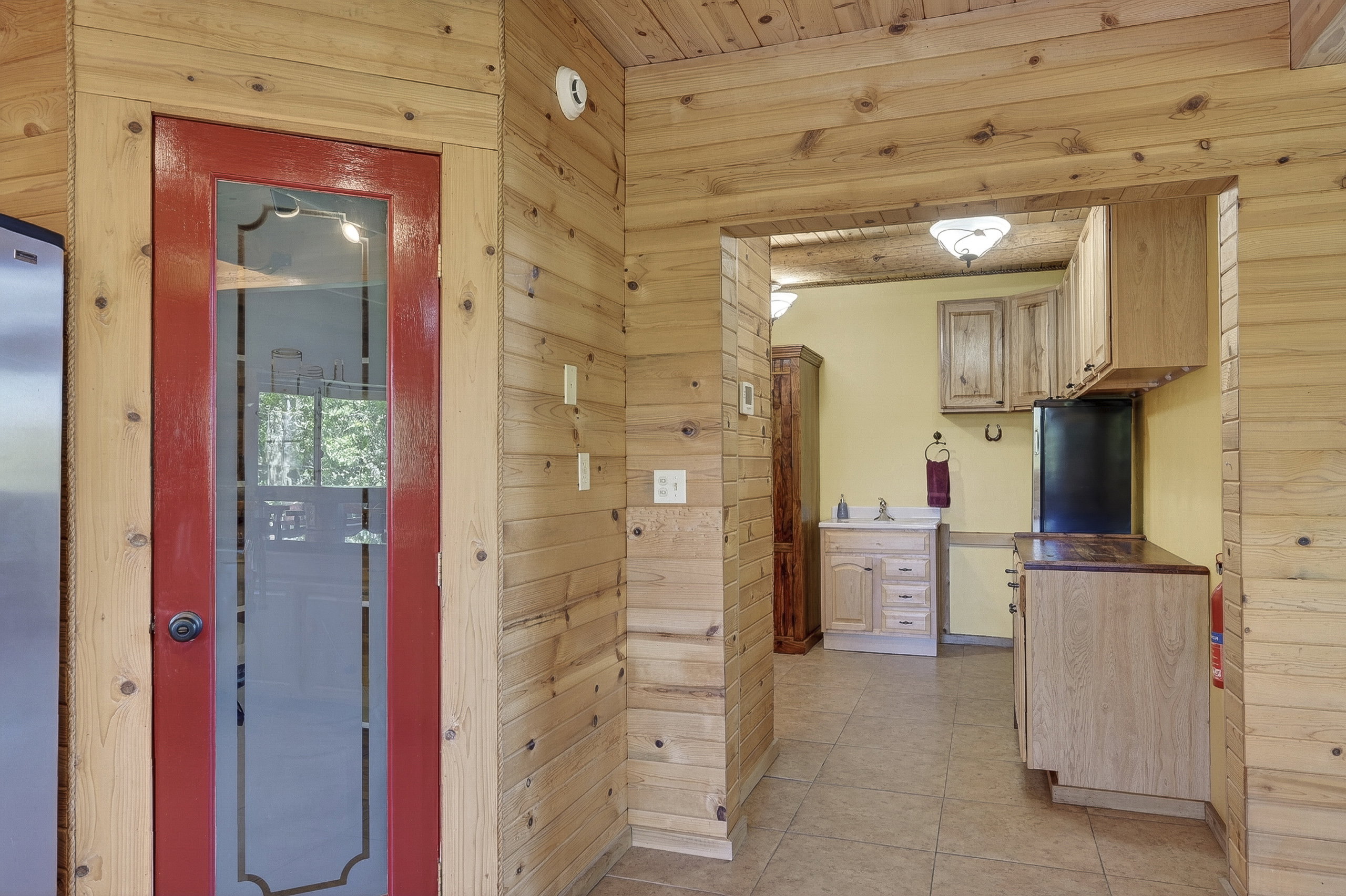 Wood-paneled interior featuring a red-framed glass door, tiled flooring, and a kitchen area with wood cabinetry