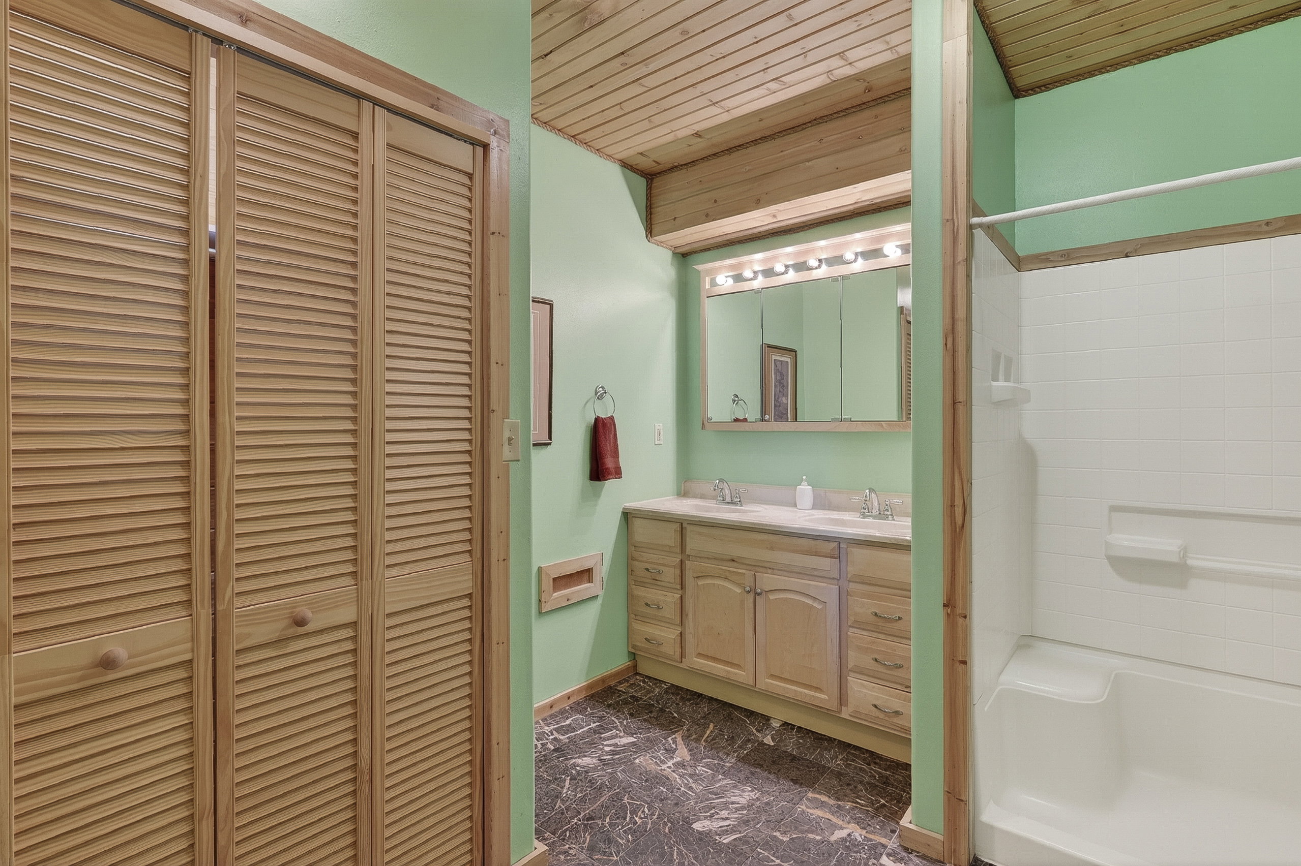 Bathroom featuring a double vanity with light wood cabinetry, a large wall-mounted mirror, and a coordinated wood-finish ceiling