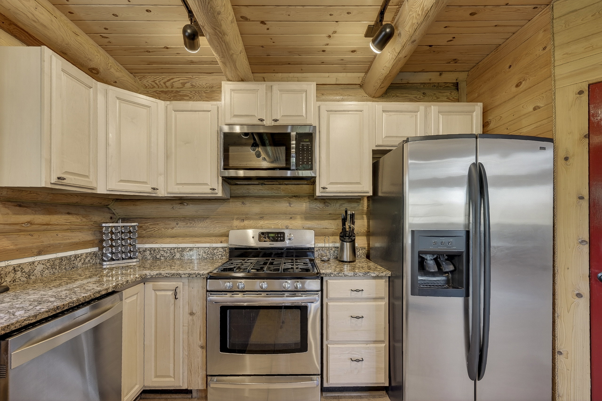 Kitchen featuring stainless steel appliances, light-toned cabinetry, natural wood-paneled walls, a wood-beam ceiling, and stone-finish countertops