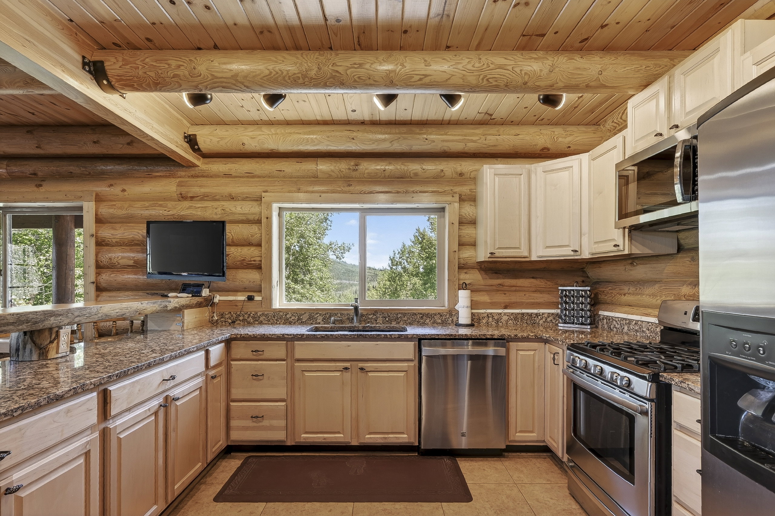 Kitchen featuring wood-paneled walls and ceiling with exposed log beams