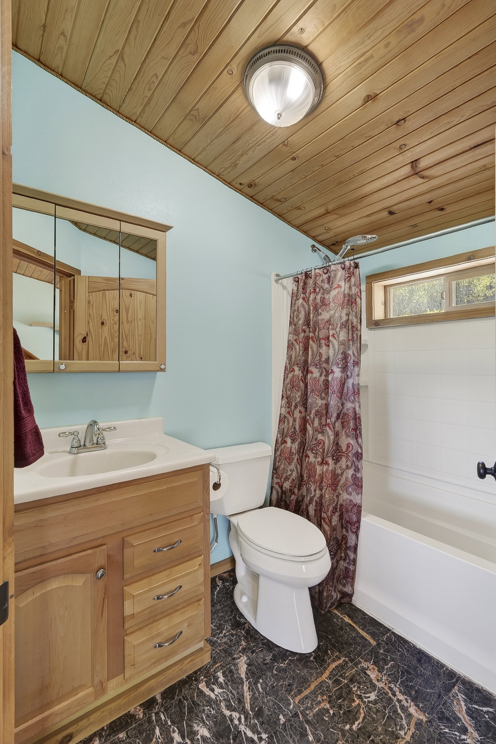 Full bathroom featuring a wood-finish plank ceiling, blue walls, a light wood vanity with a white countertop and integrated sink, a white toilet, and dark marbled-finish flooring