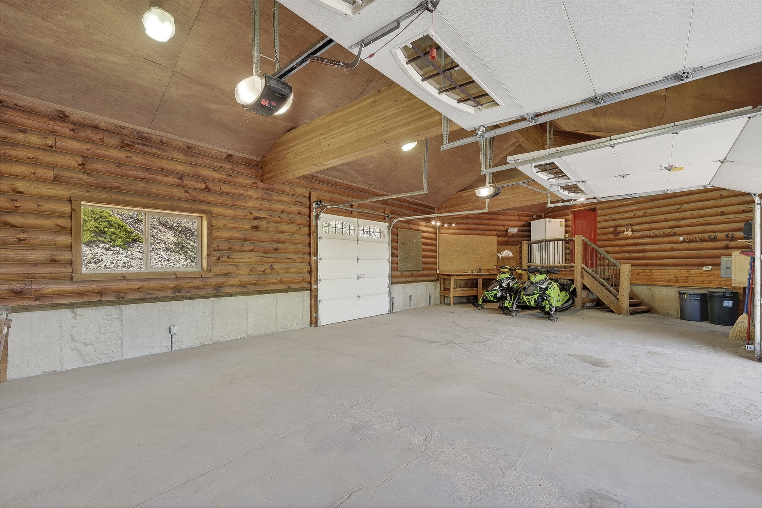Spacious garage featuring log-style walls, a concrete floor, and two overhead garage doors