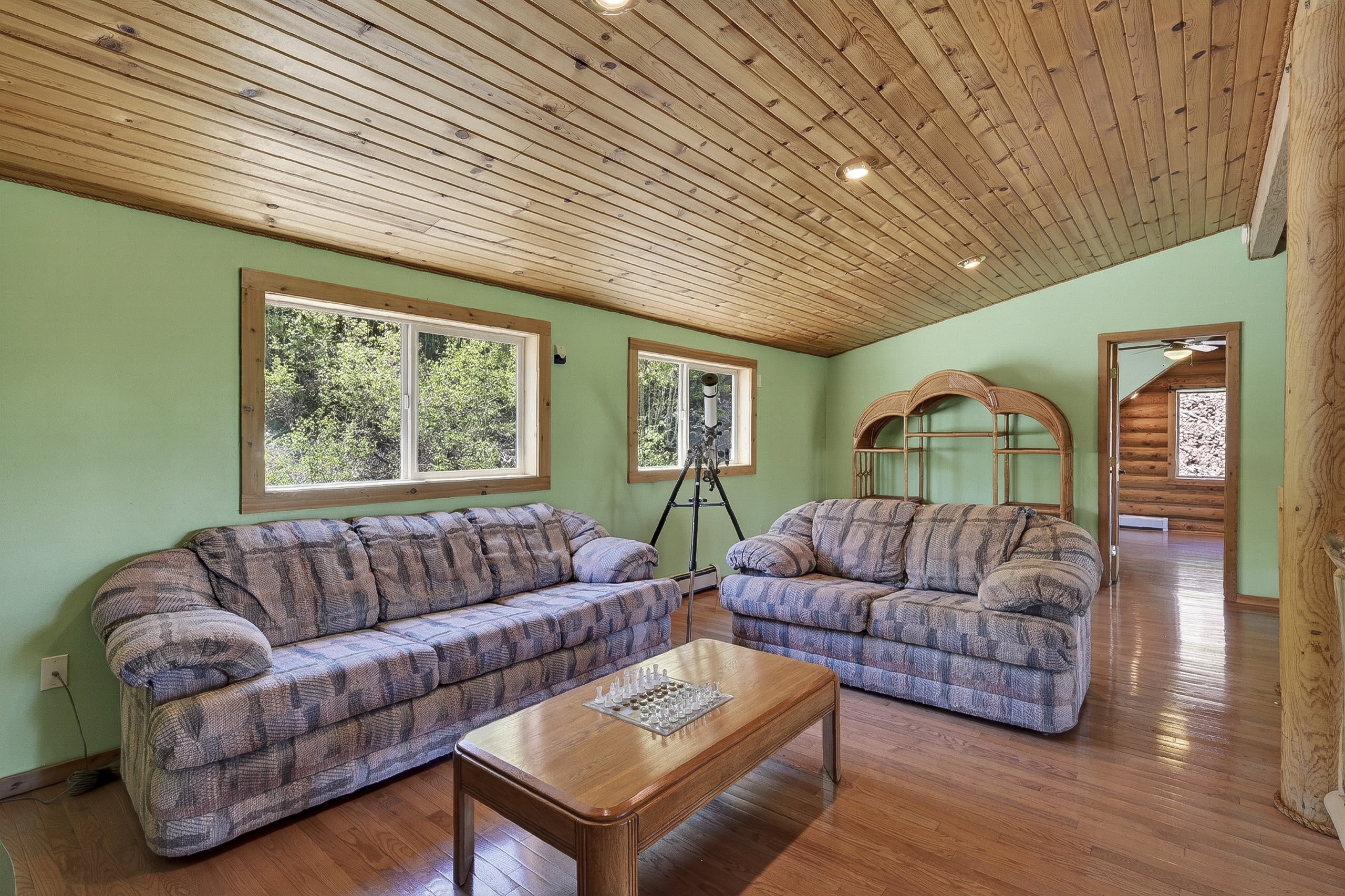 Spacious room featuring wood-finish flooring, light green walls, and a wood-paneled sloped ceiling with recessed lighting