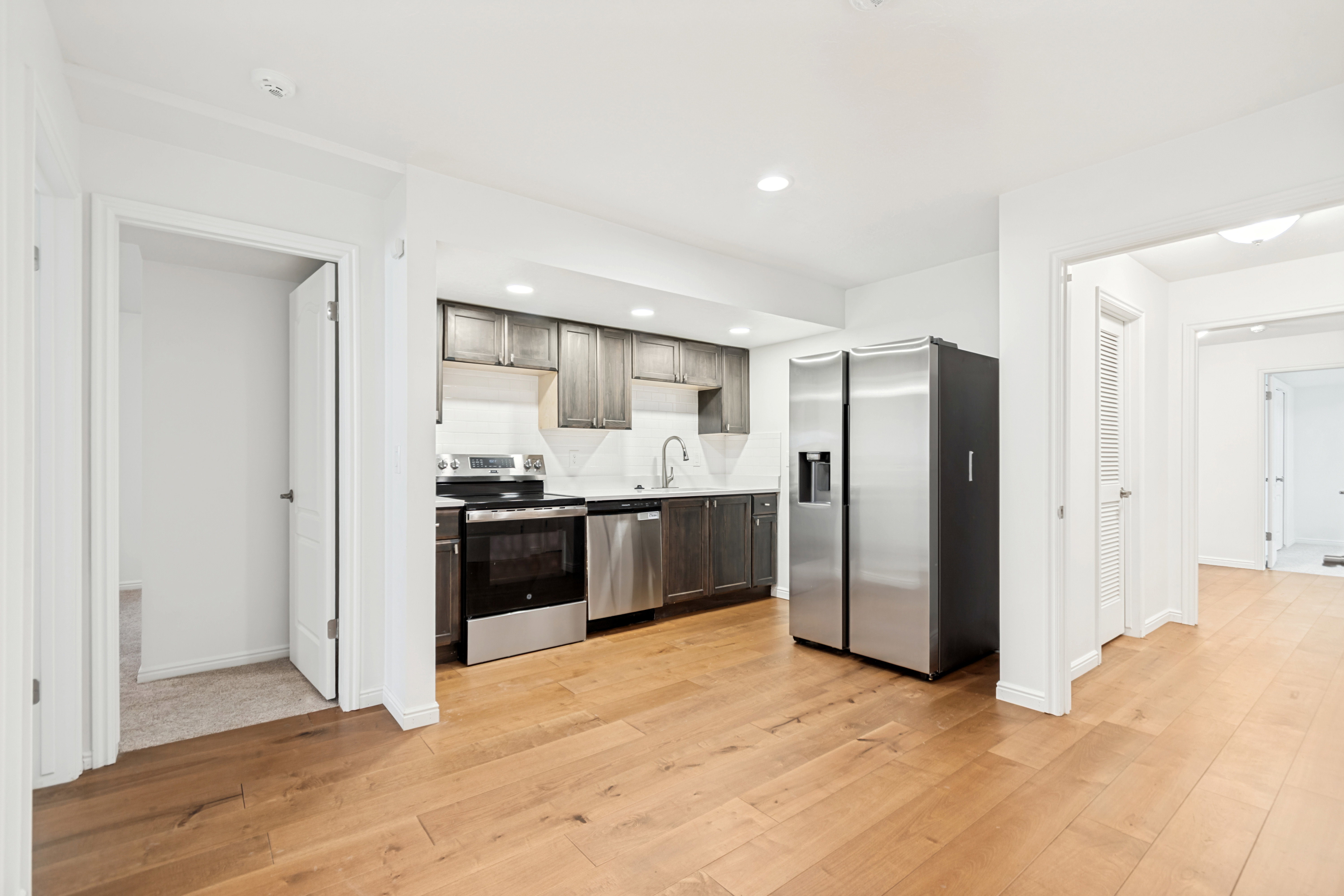 Kitchen featuring wood-finish flooring, stainless steel appliances, dark wood-tone cabinetry, white countertops, and a white subway tile backsplash