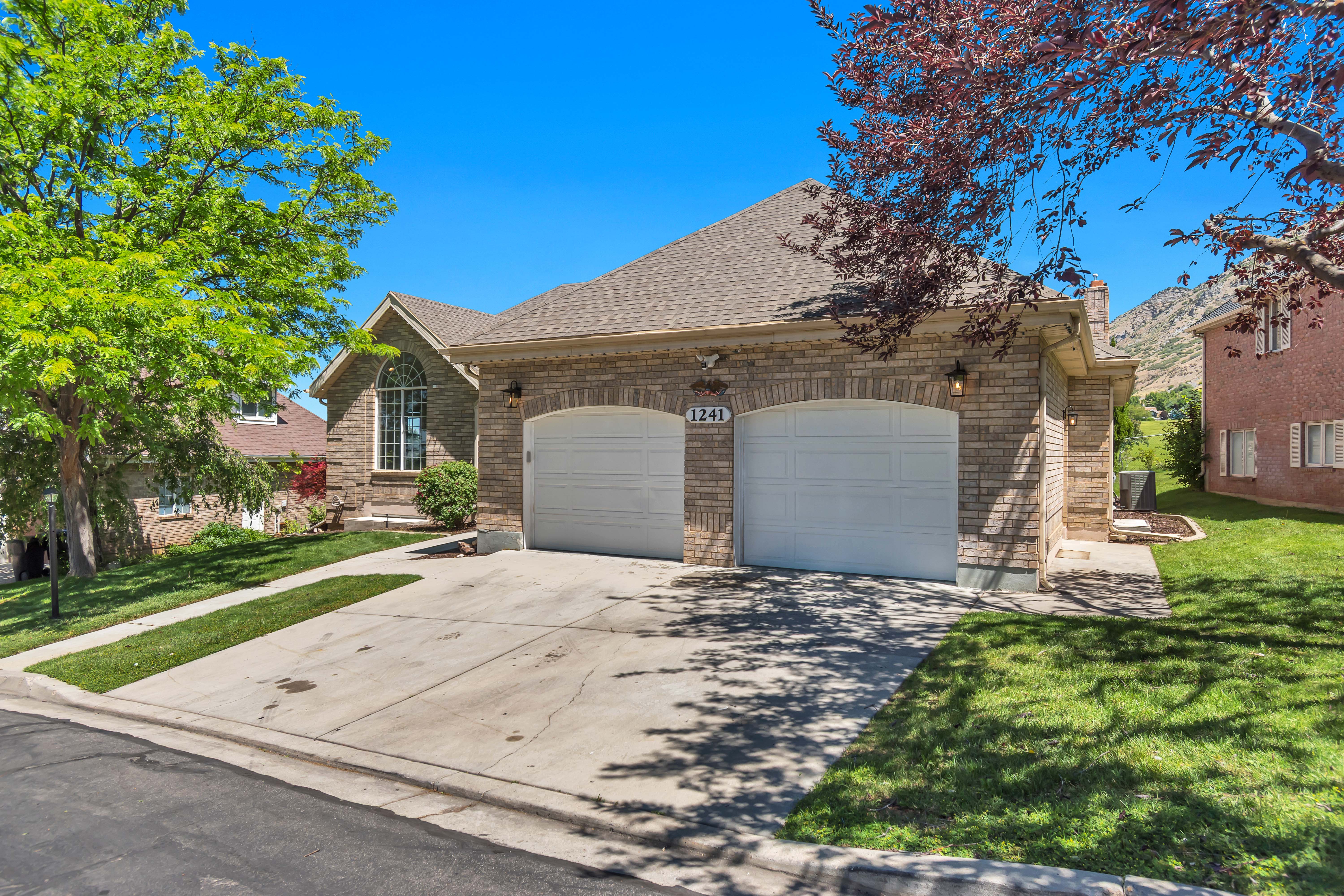 Brick facade home featuring a two-car garage with arched entrances, a pitched shingle roof, a prominent arched window, and landscaped front yard