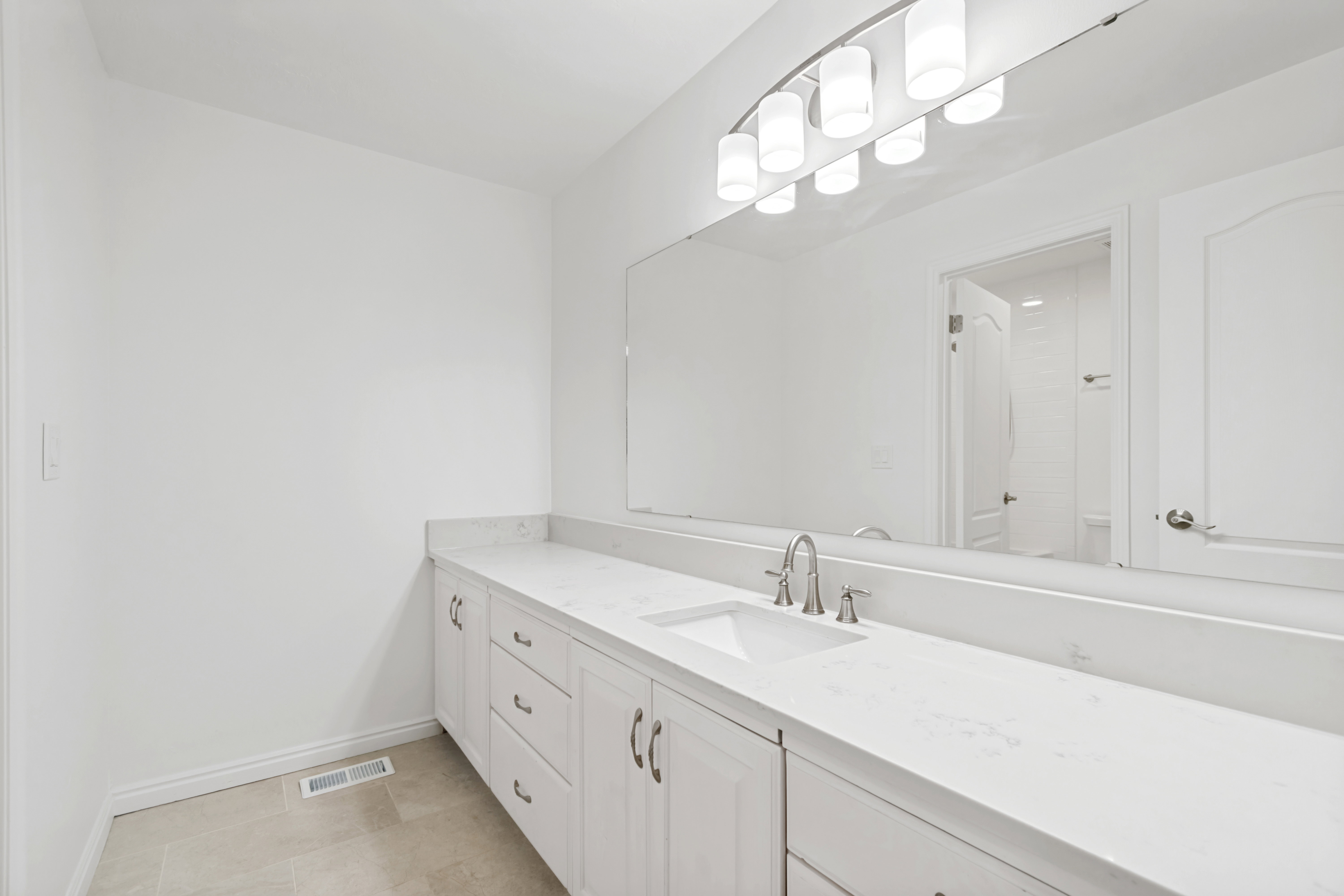 Spacious vanity featuring double sinks with brushed nickel fixtures, extensive countertop space, white cabinetry, a large wall-mounted mirror, and an overhead five-light fixture