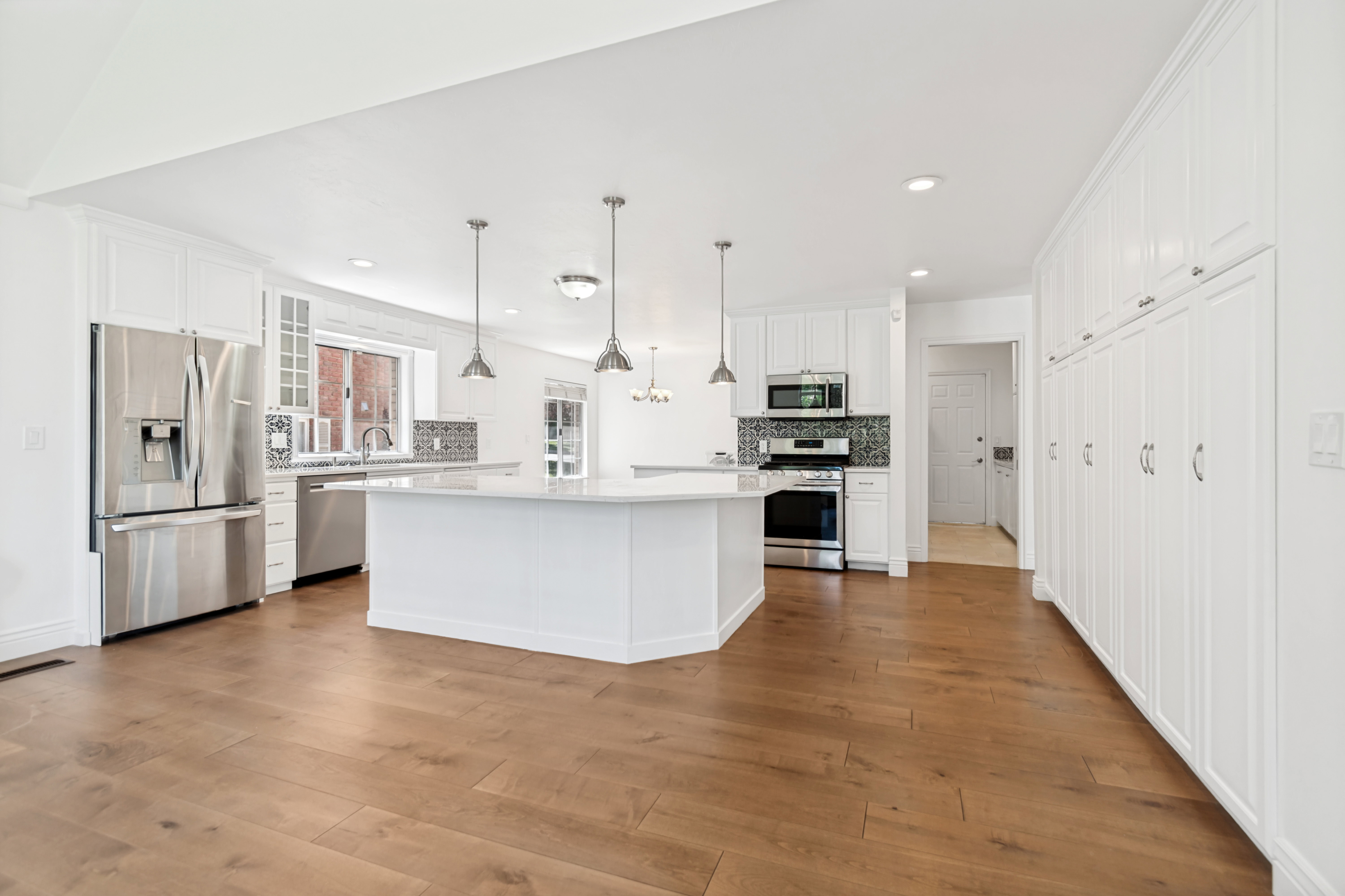 Spacious kitchen featuring an expansive center island with seating, stainless steel appliances, abundant white cabinetry, wood-finish flooring, and a decorative tile backsplash