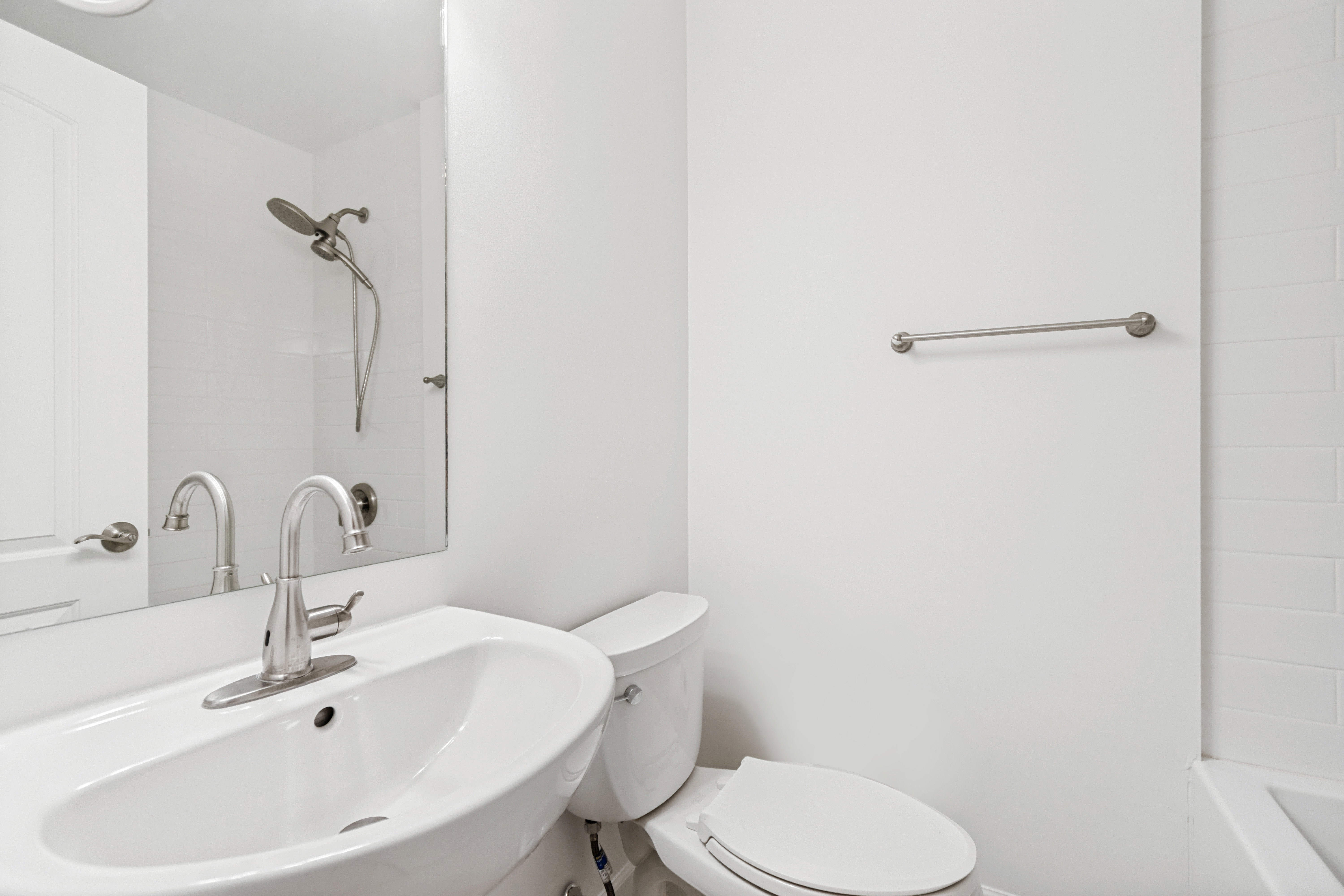 Modern bathroom featuring a white ceramic pedestal sink with a brushed nickel faucet, a white toilet, and a bathtub with white subway tile surround and a brushed nickel shower head