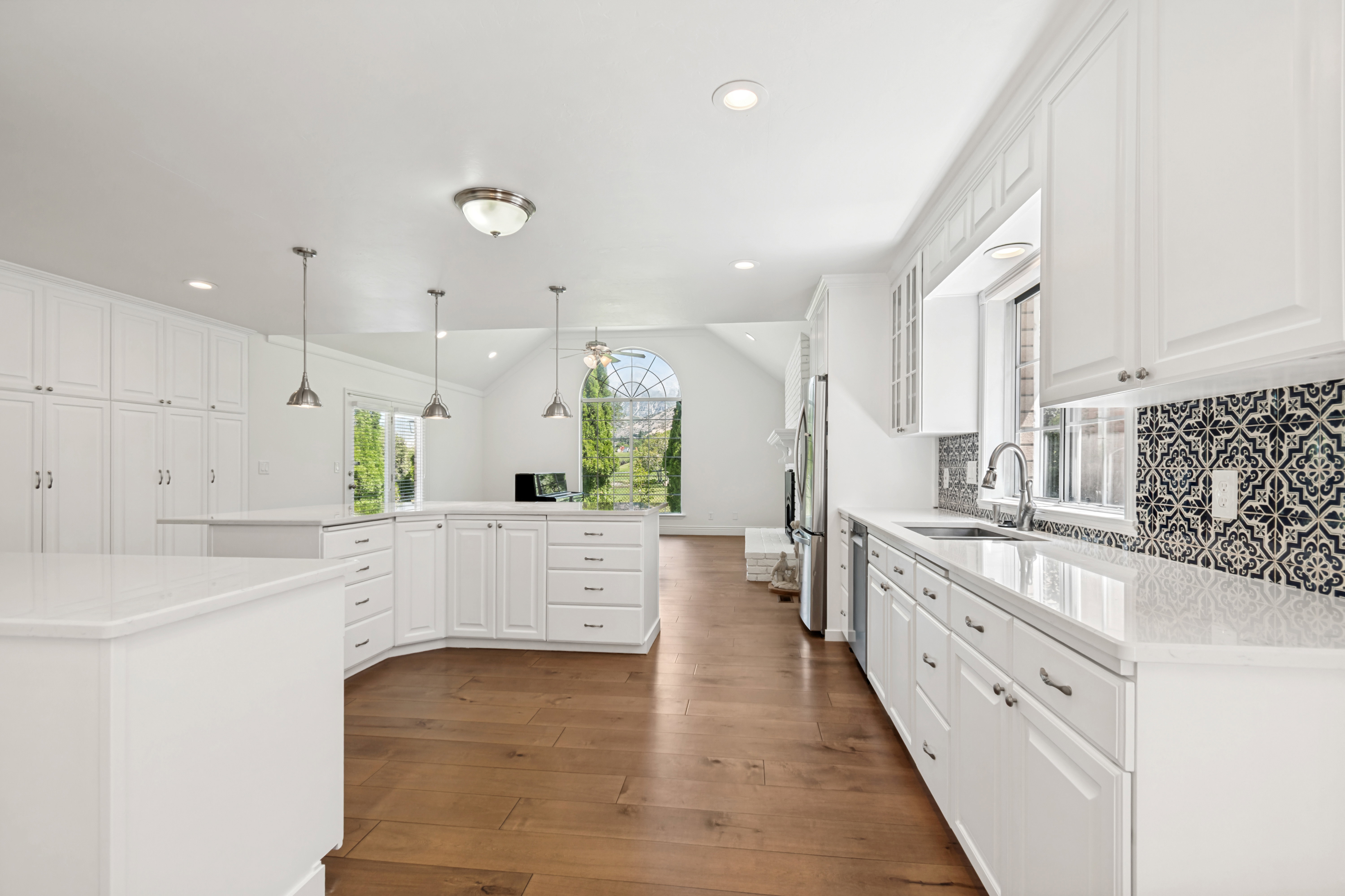 Spacious kitchen featuring white cabinetry, light countertops, wood-finish flooring, patterned backsplash, and stainless steel appliances