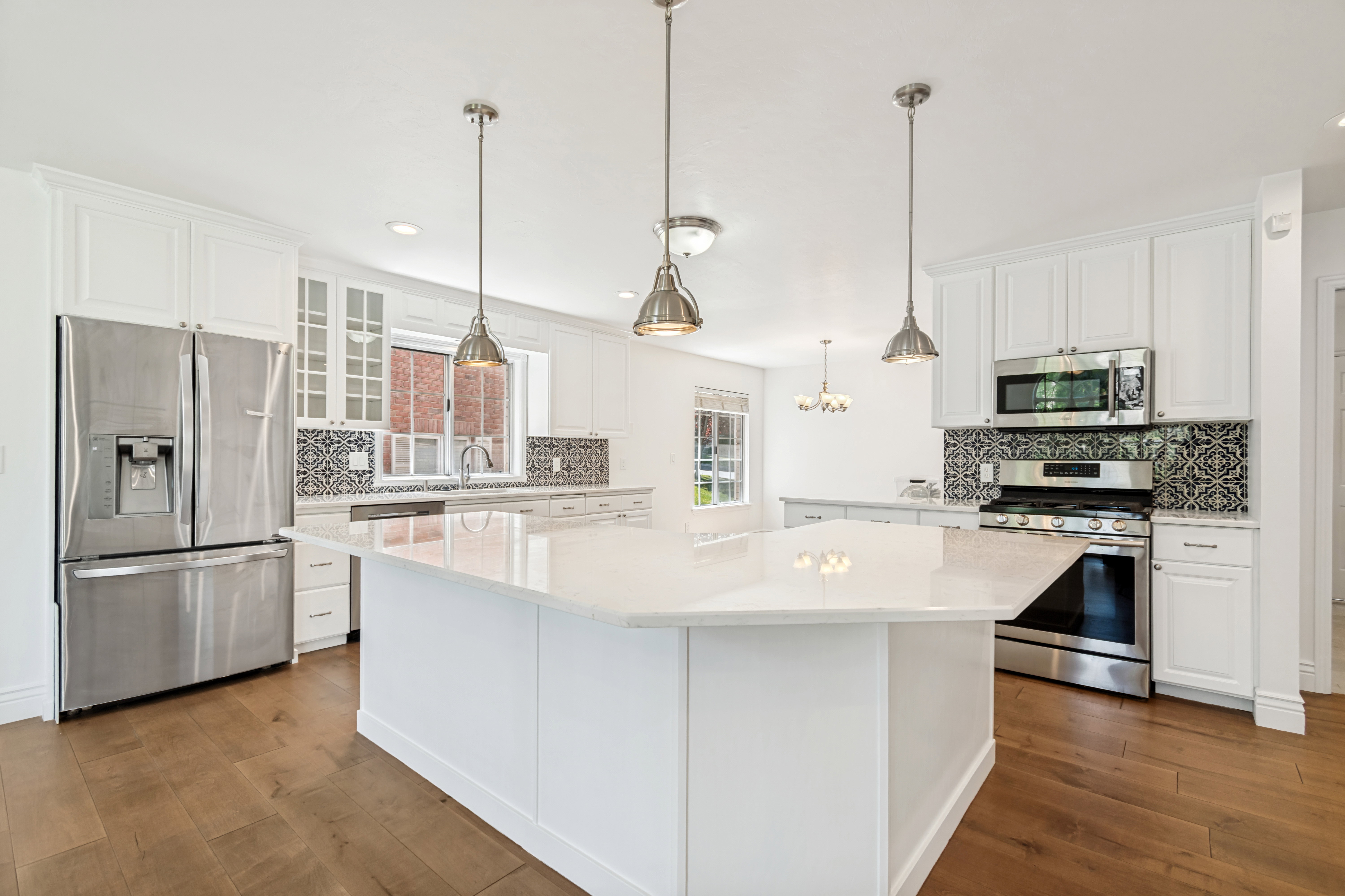 Spacious kitchen featuring an expansive central island with a light-toned countertop, white cabinetry, stainless steel appliances, and wood-finish flooring