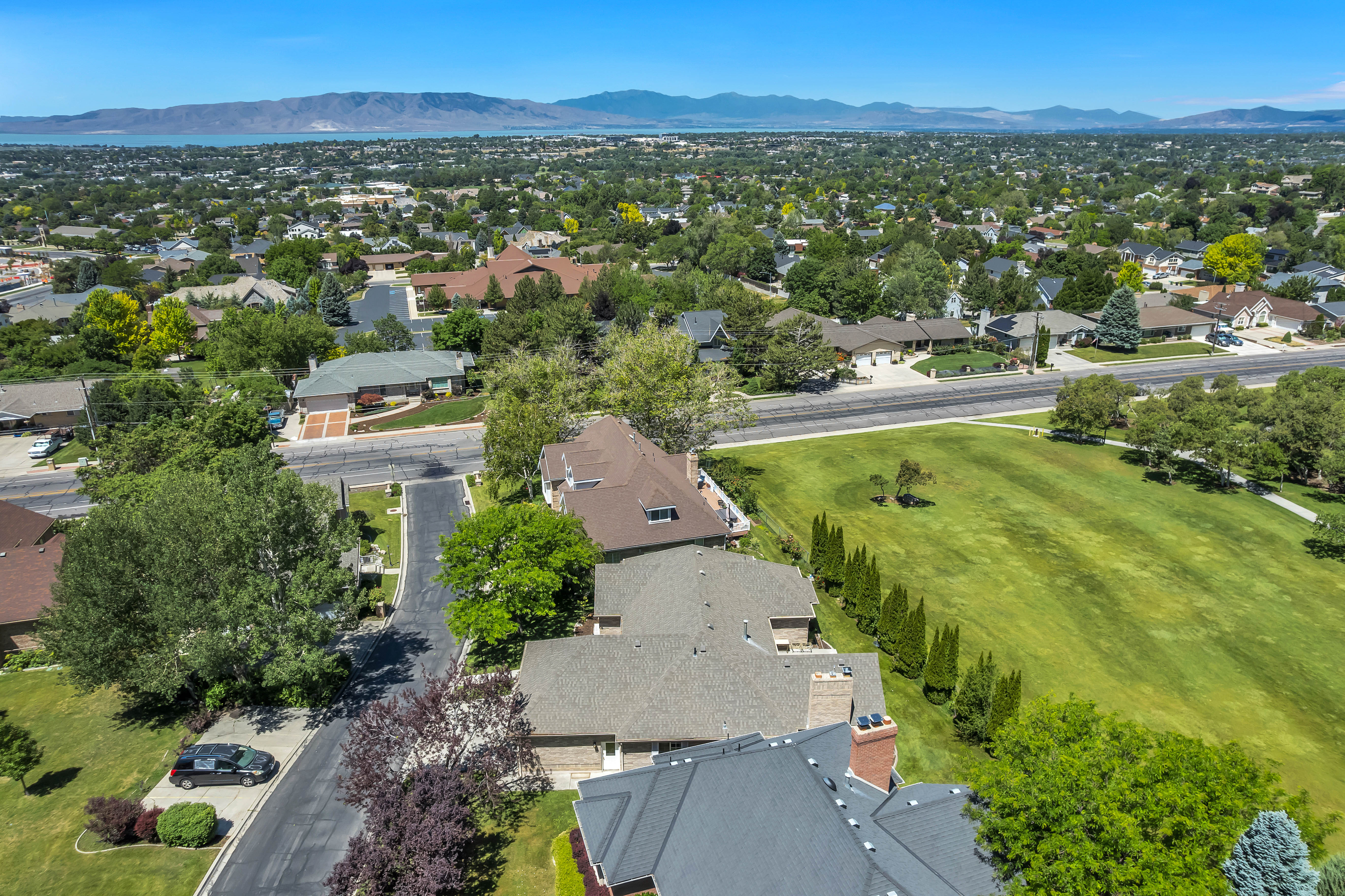 Expansive neighborhood featuring mature trees, residential properties, a golf course, and distant mountains with a body of water