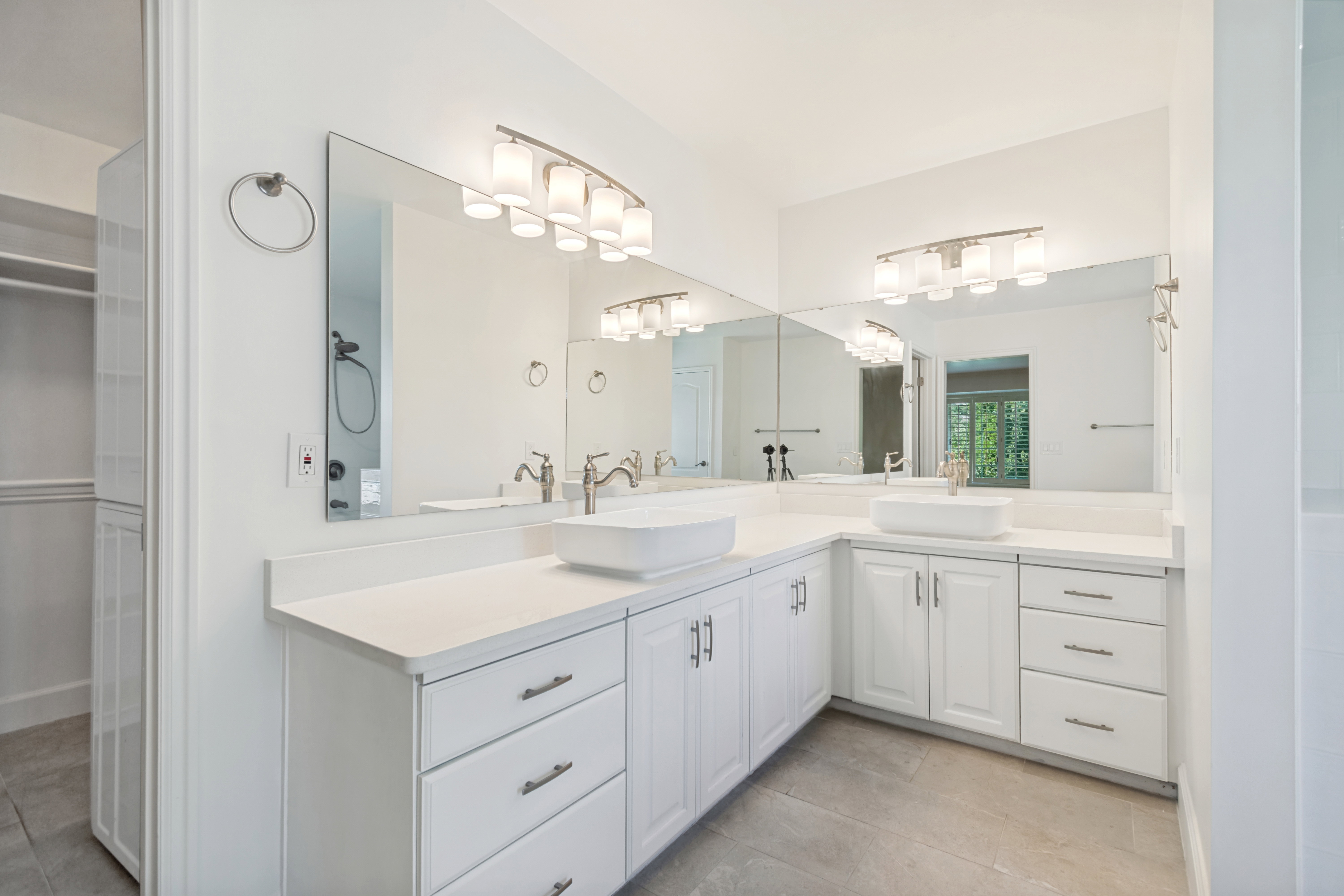 Dual vessel sinks with brushed nickel fixtures, under-mount cabinetry, expansive vanity countertop, wall-mounted mirrors, and contemporary light fixtures