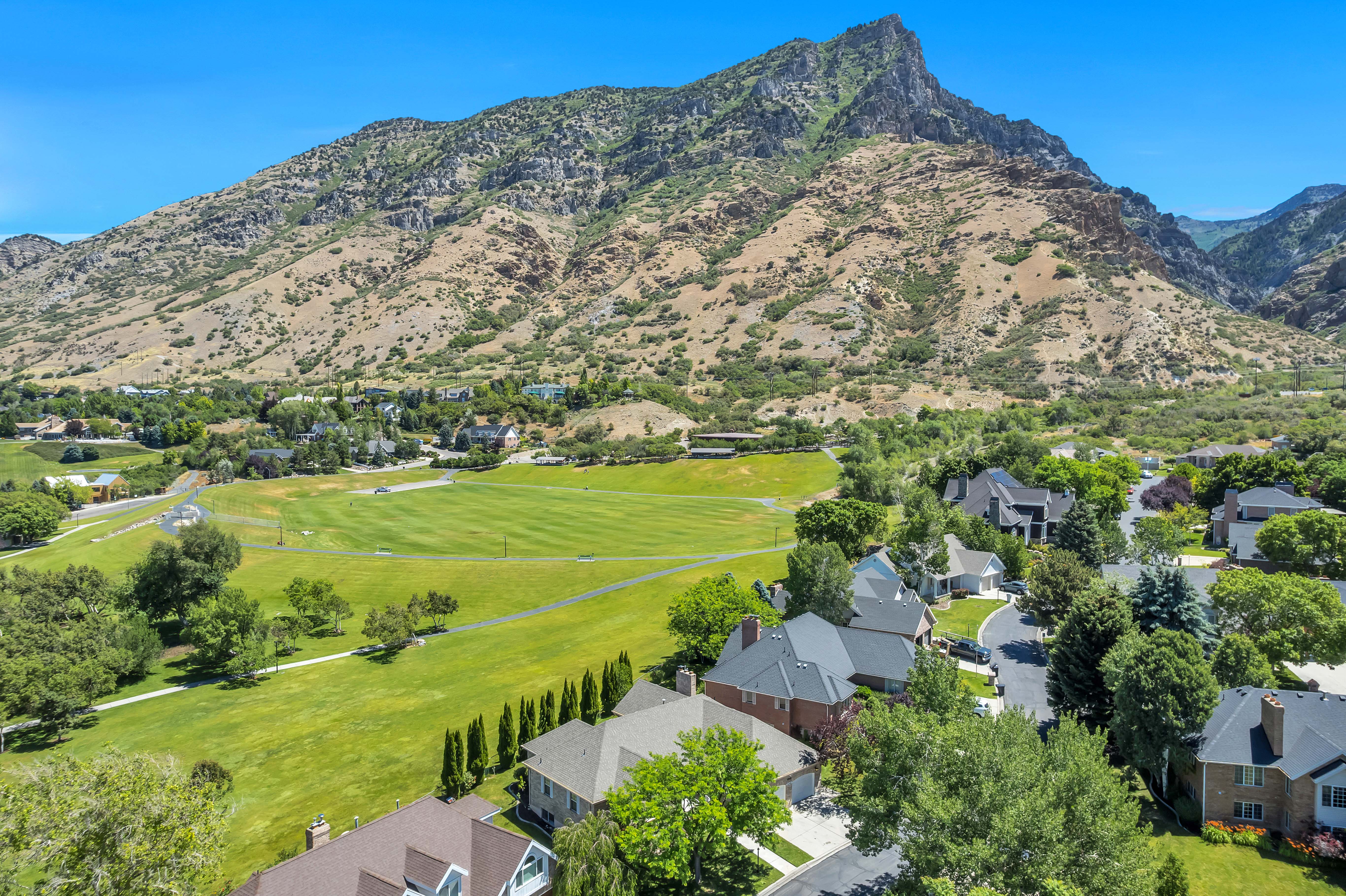 Residential area with varied architectural styles and established landscaping, bordered by expansive green spaces and a prominent mountain range