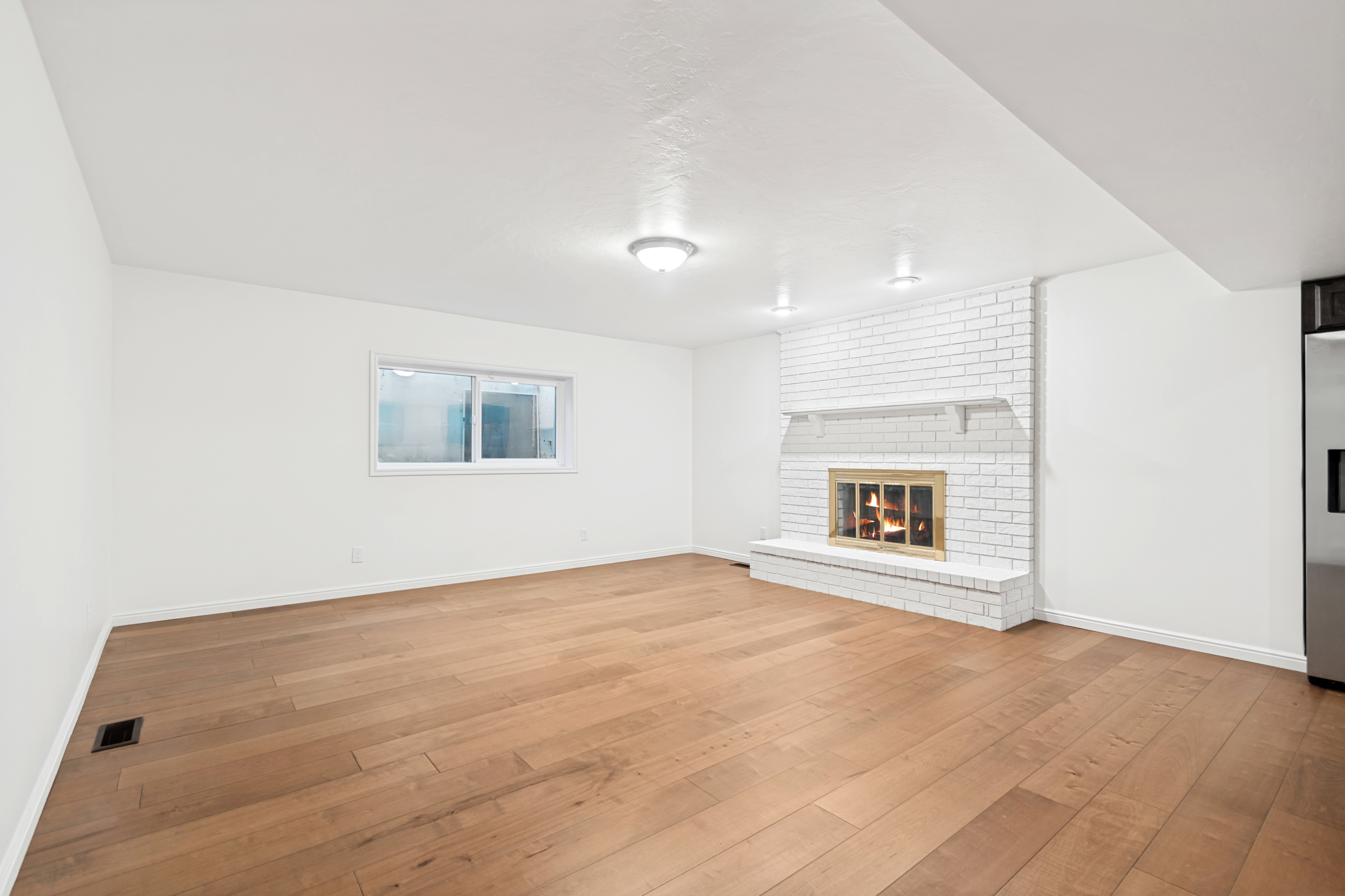 Spacious room featuring wood-finish flooring, a white painted brick fireplace with a mantel, and built-in ceiling lighting