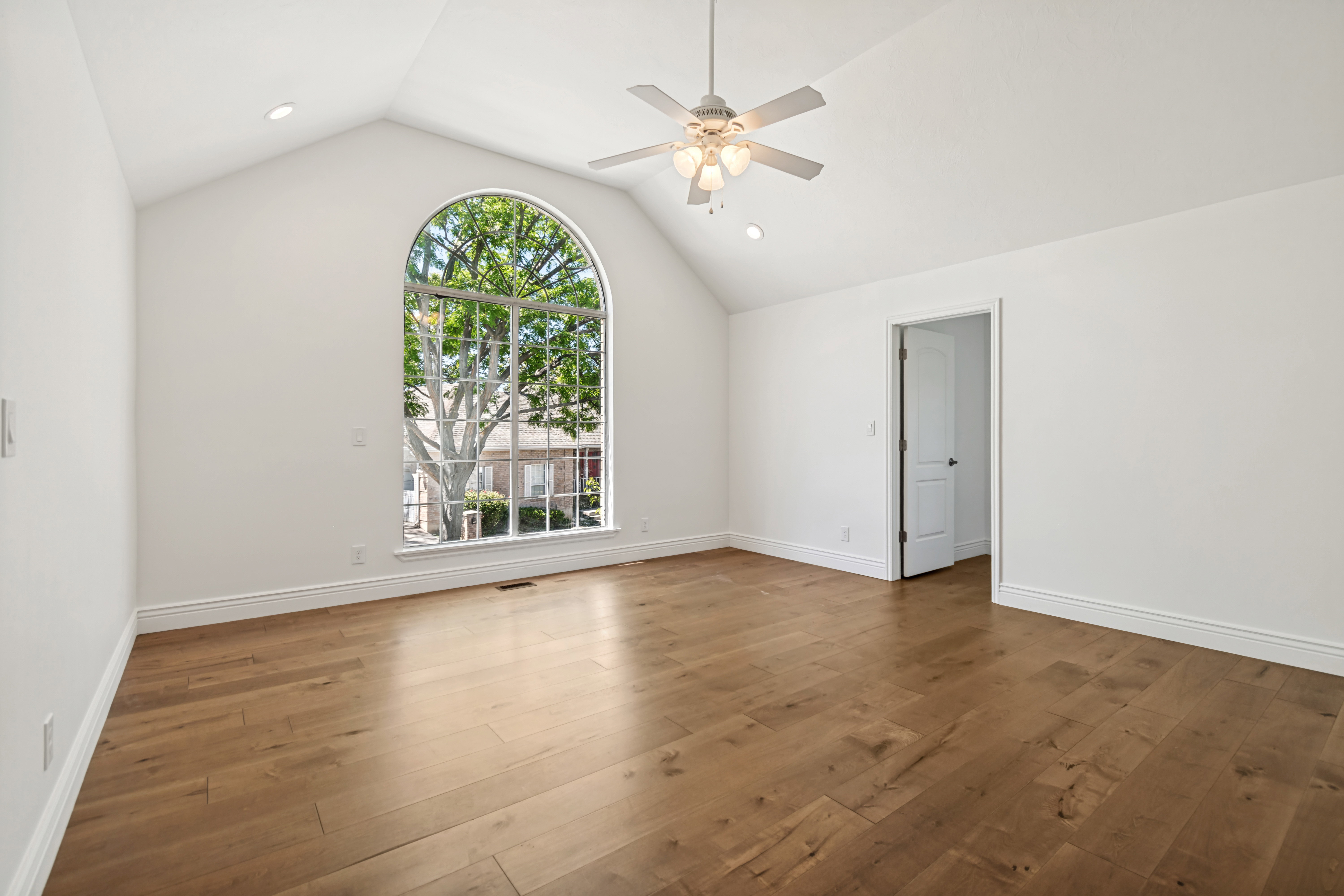 Vaulted ceiling room featuring an arched window, wood-finish flooring, a ceiling fan with integrated lighting, and recessed lighting