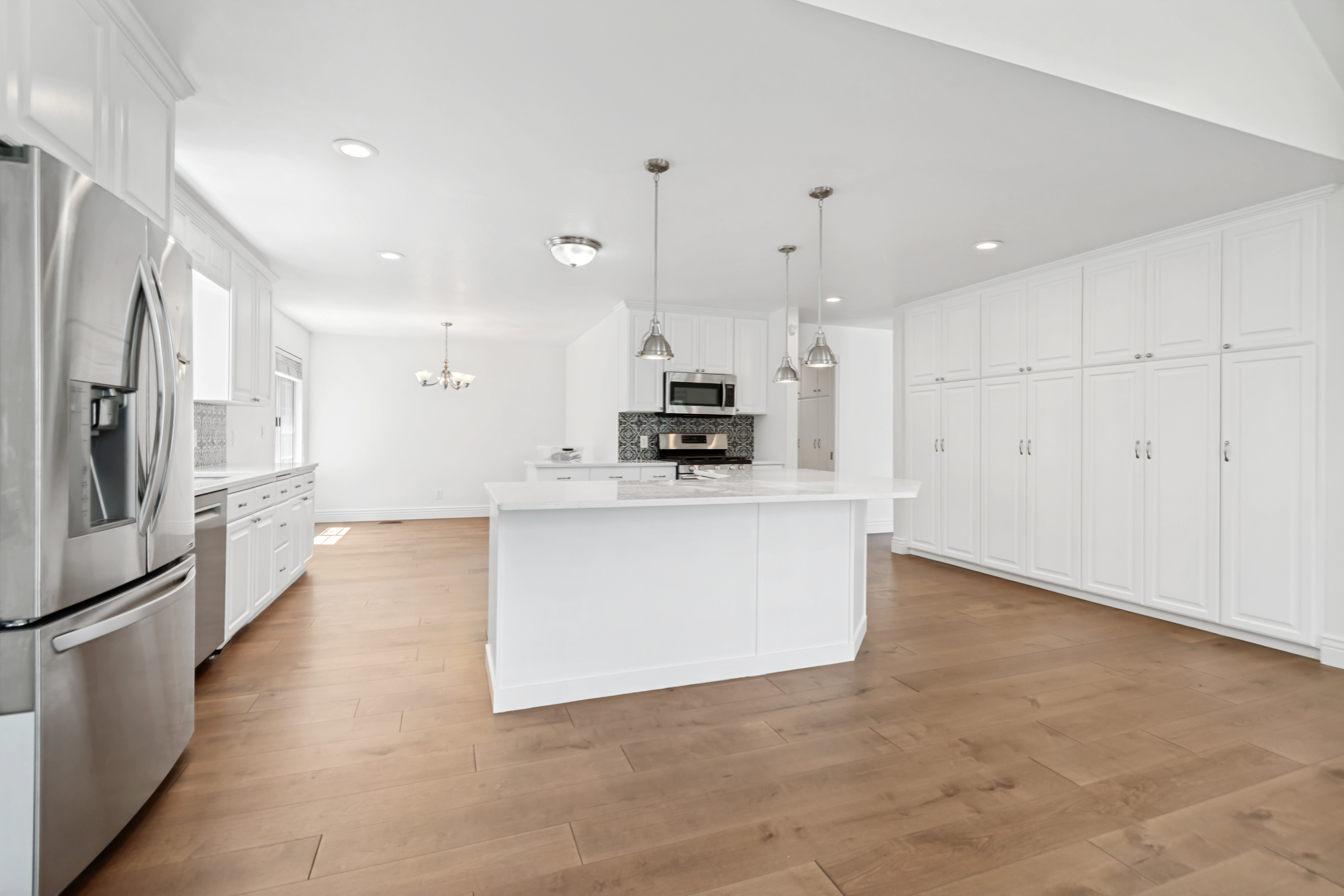 Open-concept kitchen featuring an oversized island with countertop seating, white shaker cabinetry, stainless steel appliances, and wood-finish flooring