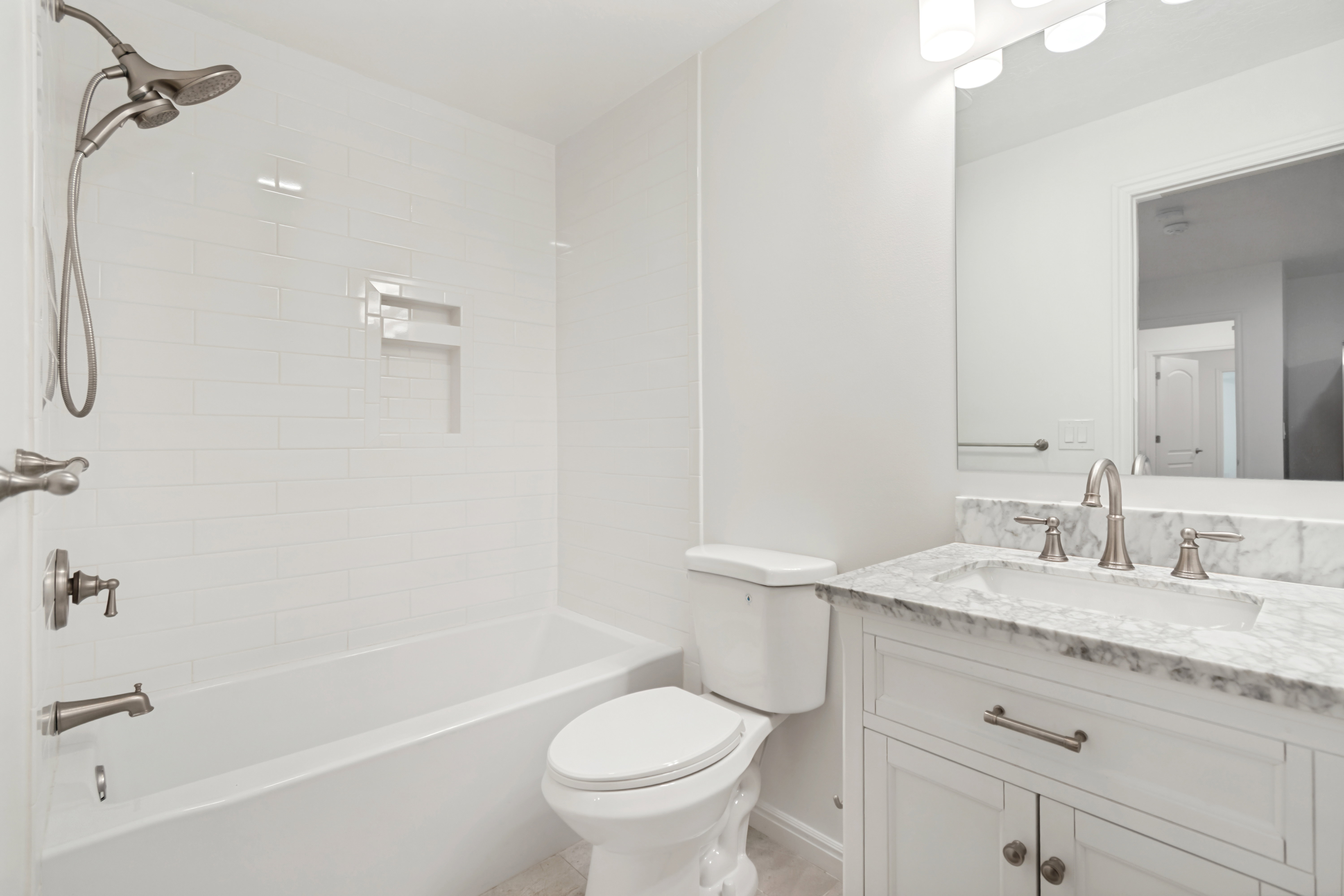 Bathroom featuring a built-in tub with subway tile surround, recessed shower niche, brushed nickel shower fixtures, white vanity with stone countertop, and an undermount sink