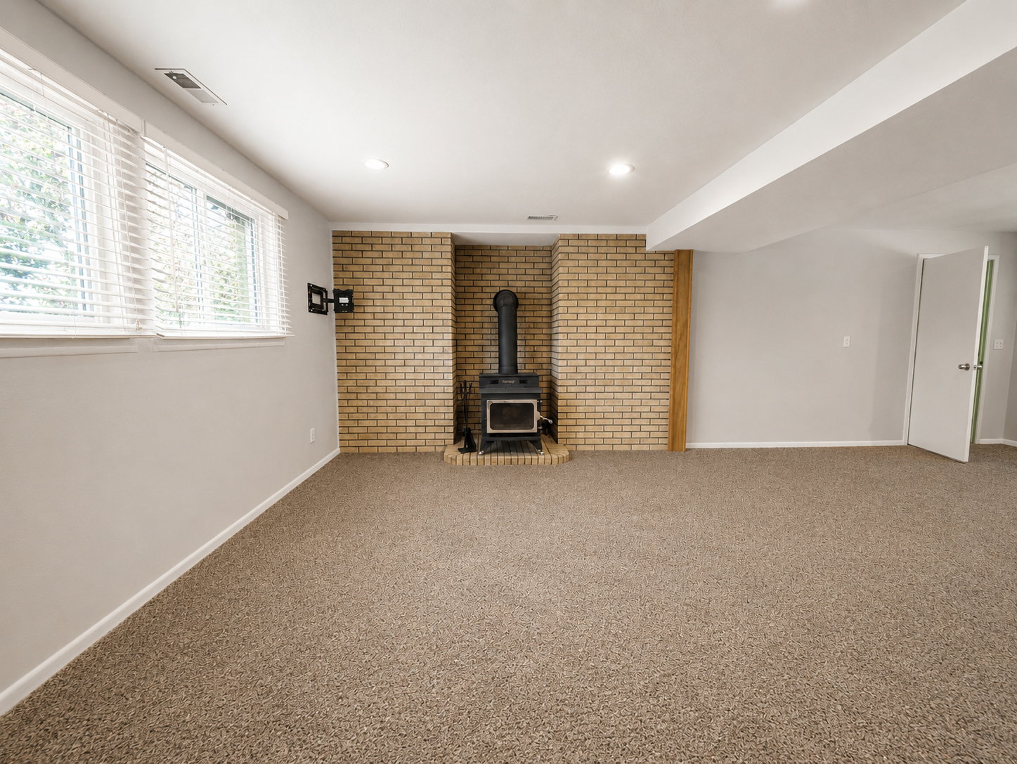 Spacious room featuring a brick-clad wood stove, multiple windows with blinds, light gray wall paint, and recessed ceiling lighting