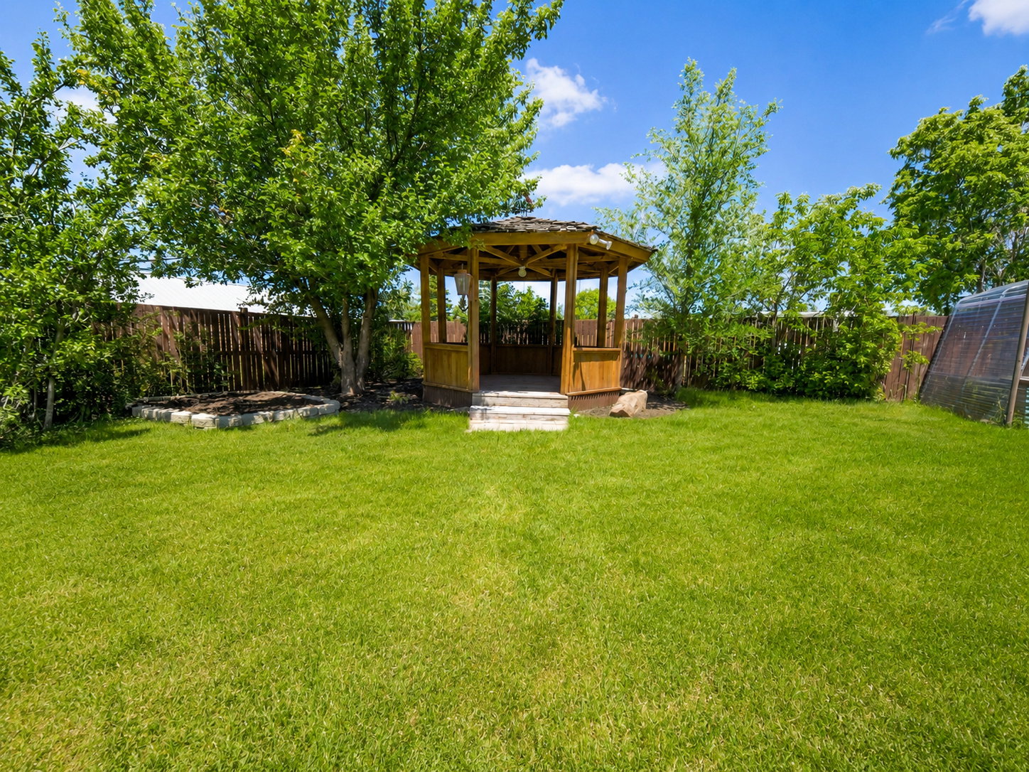 Expansive backyard featuring a wood gazebo with white steps, surrounded by mature trees