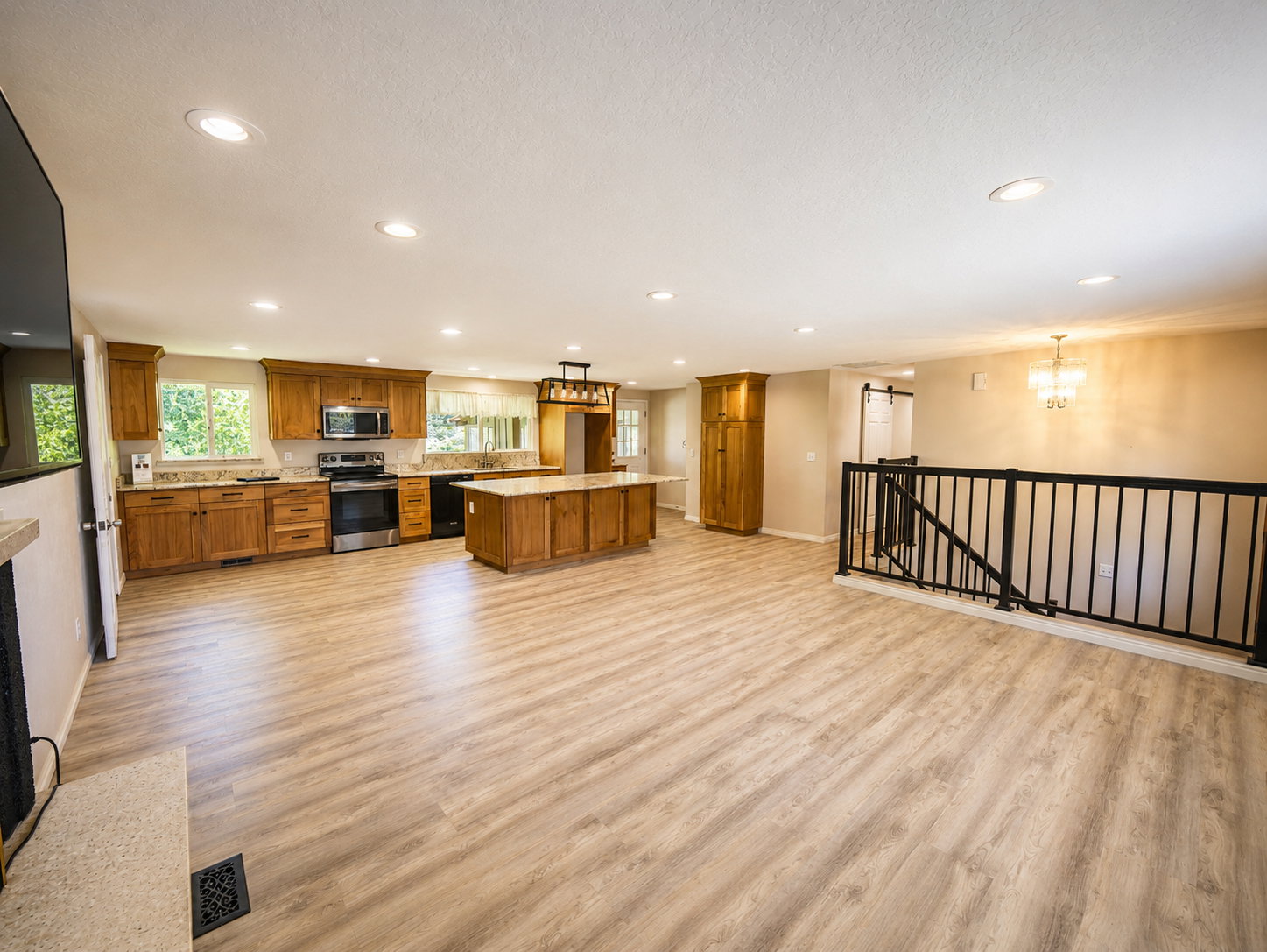 Open-concept living space featuring wood-finish flooring, recessed lighting, and a kitchen with wood cabinetry, stainless steel appliances, and a central island with a stone-look countertop