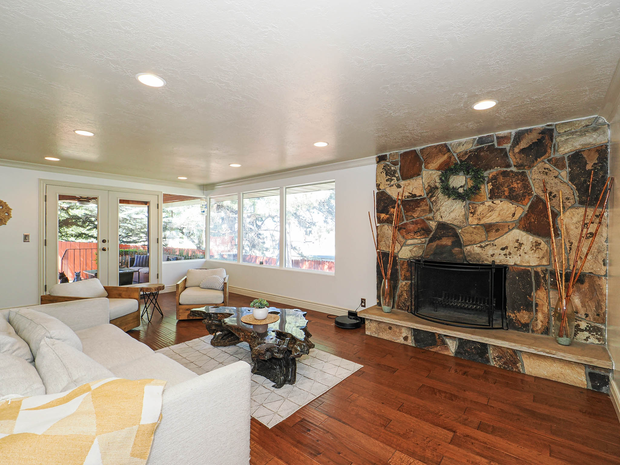 Living area featuring a floor-to-ceiling stone fireplace, rich wood-finish flooring, recessed lighting, and expansive windows
